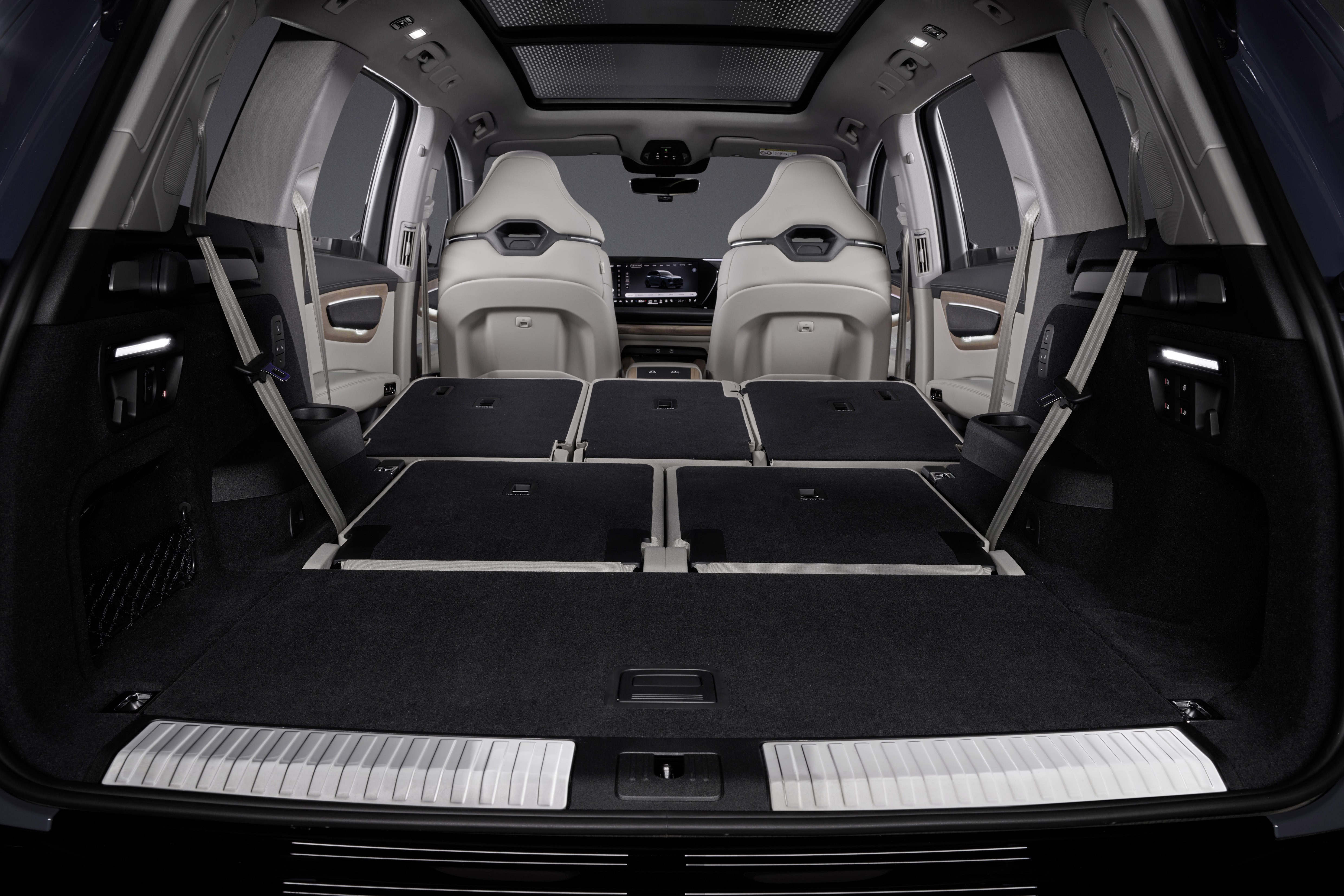 Interior de um SUV com a terceira e segunda fileiras de bancos rebatidas, criando um amplo espaço de carga. Os bancos dianteiros são brancos, e o teto solar panorâmico é visível.