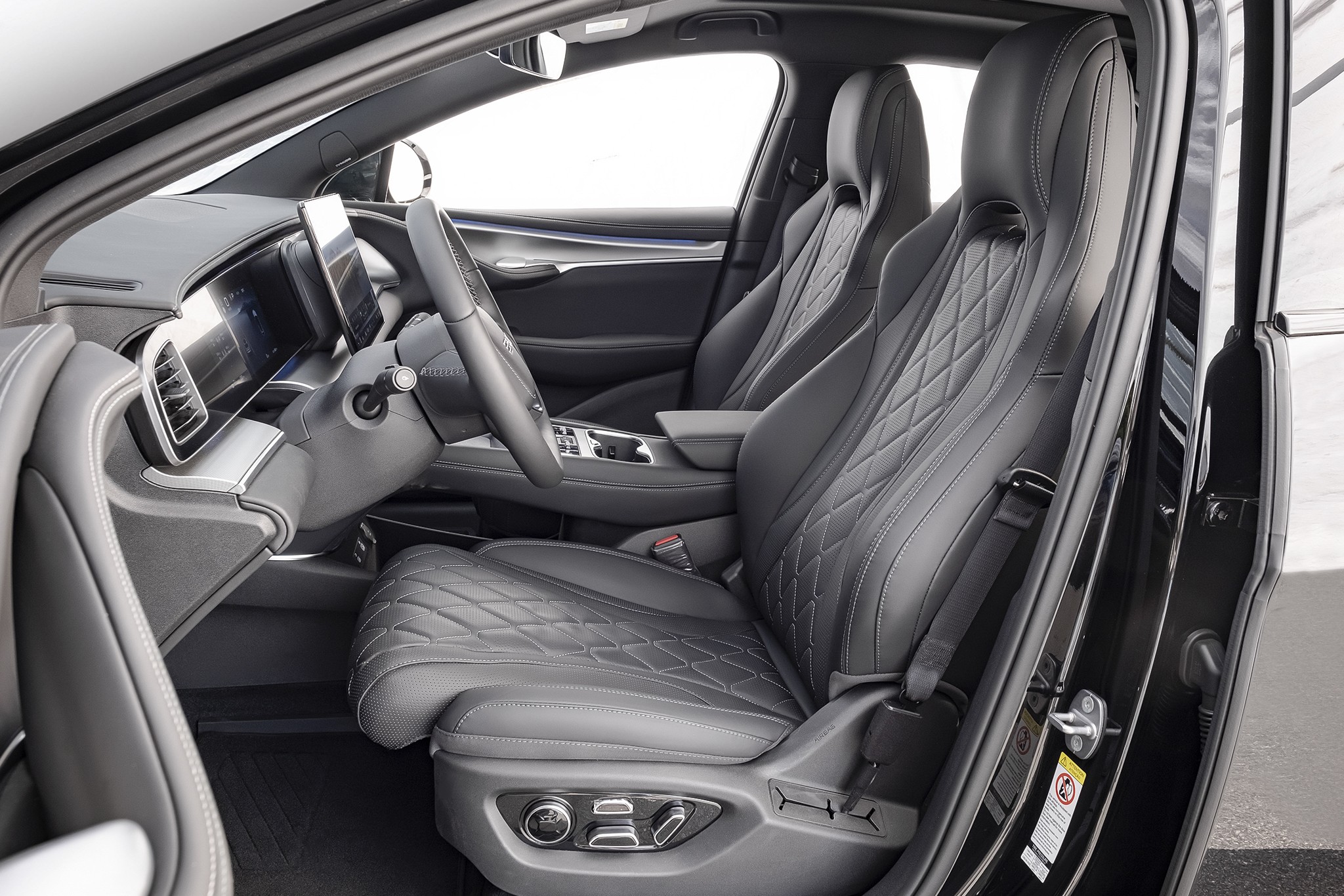 Interior de carro moderno com bancos de couro cinza escuro e costura em losango, volante multifuncional, painel digital e tela central. A porta do motorista está aberta, revelando o acabamento preto e detalhes cromados. O ambiente é sofisticado e tecnológico