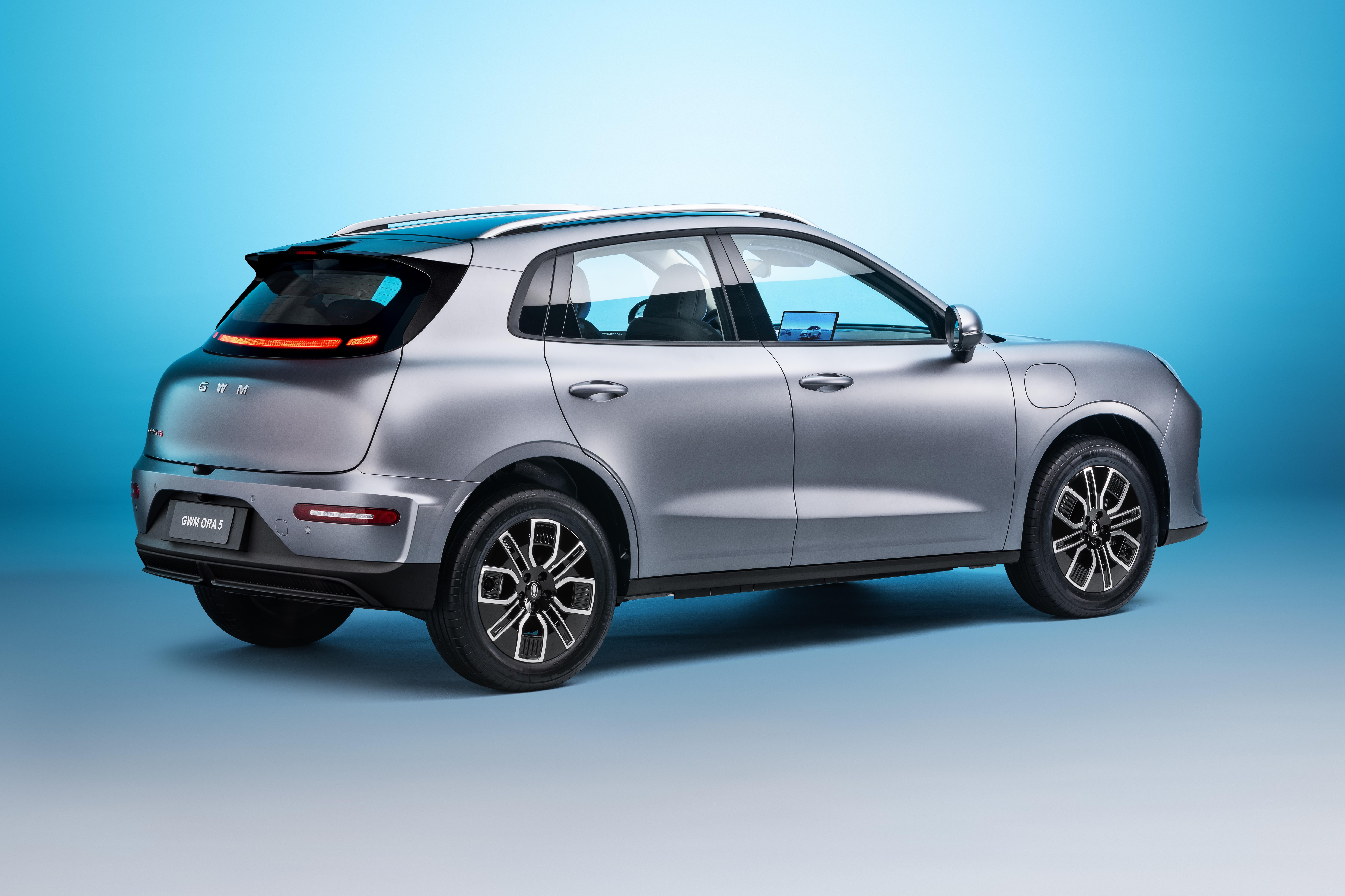 SUV elétrico cinza-prateado, visto de três quartos traseiro, com teto solar panorâmico, lanternas traseiras em LED e rodas pretas com detalhes brancos, sobre fundo azul degradê