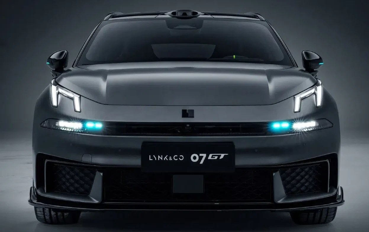 Carro Lynk & Co 07 GT cinza escuro, visto de frente, com faróis e luzes diurnas acesas em branco e azul claro, em um estúdio escuro