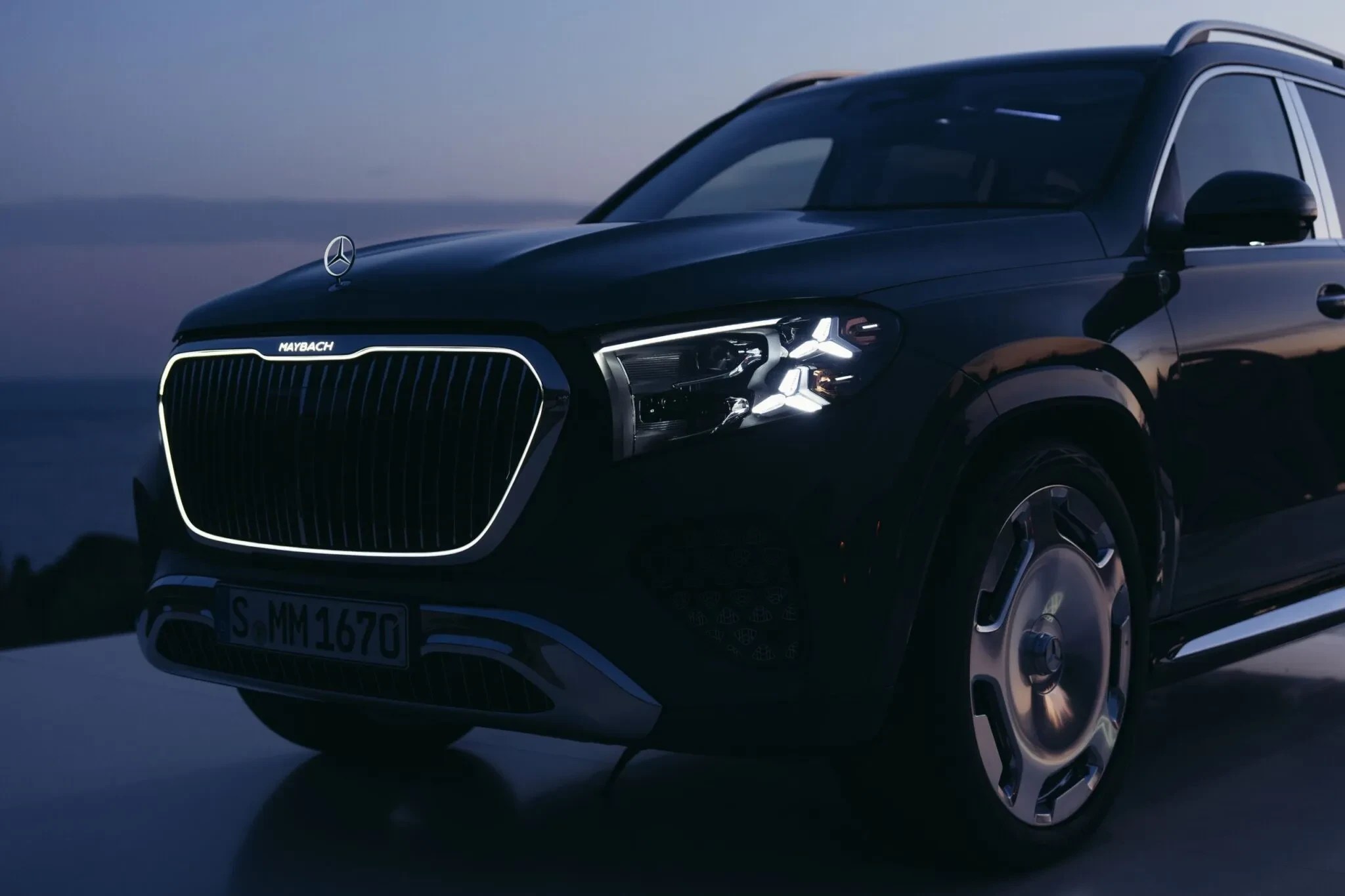 SUV Mercedes-Benz Maybach escuro, com grade frontal iluminada e faróis acesos, estacionado ao ar livre ao entardecer