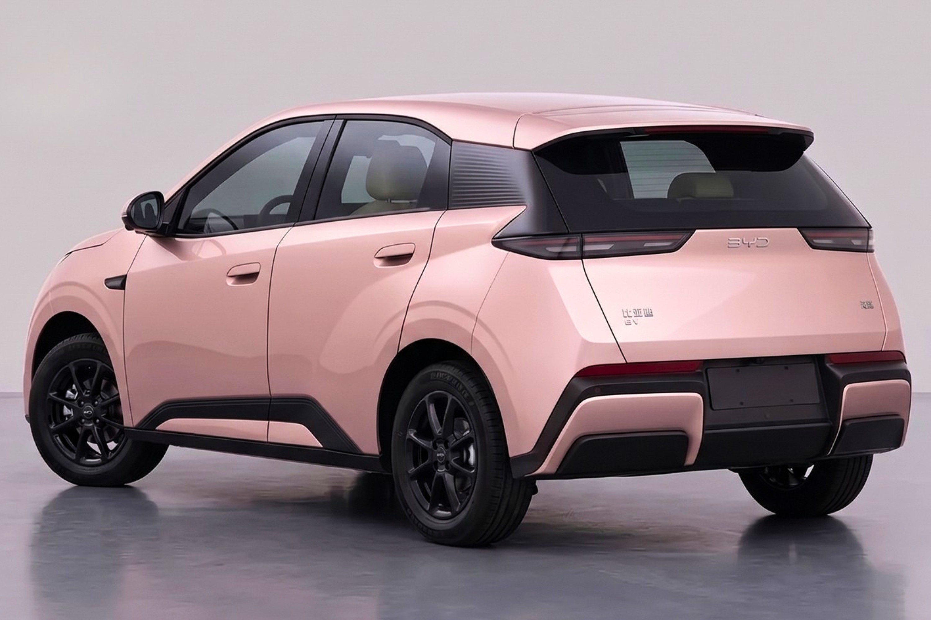 Carro compacto elétrico rosa-claro com detalhes em preto, visto de traseira e lateral, sobre piso cinza. Possui rodas pretas, lanternas traseiras horizontais e para-choque com apliques pretos e rosa.