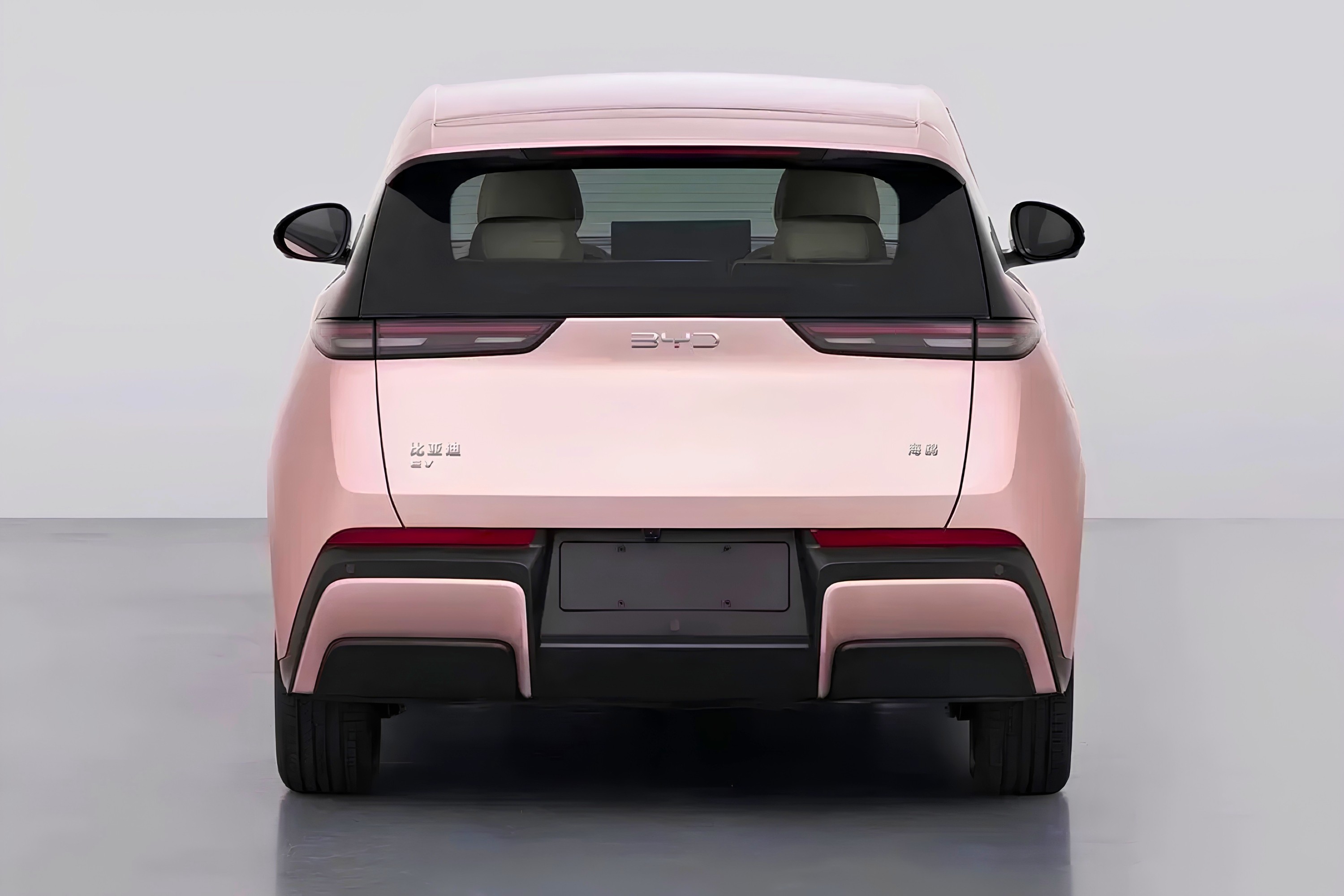 Traseira de um carro elétrico BYD Seagull rosa claro, com lanternas horizontais finas e o nome da marca em destaque. O para-choque tem detalhes em preto e rosa, e o vidro traseiro escuro revela os encostos de cabeça dos bancos. O veículo está em um estúdio com fundo cinza claro