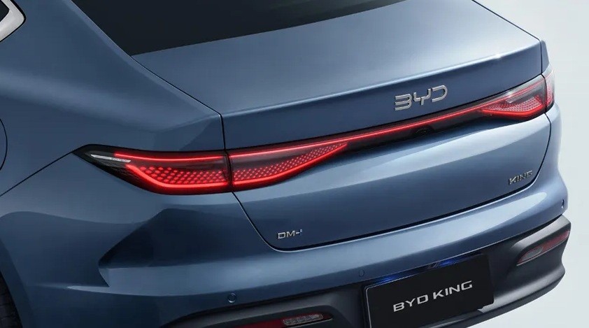 Traseira de um carro azul-marinho, com lanternas vermelhas acesas em uma barra horizontal que atravessa a tampa do porta-malas. O logotipo BYD está acima da barra de luz, e BYD KING aparece na placa preta abaixo do para-choque