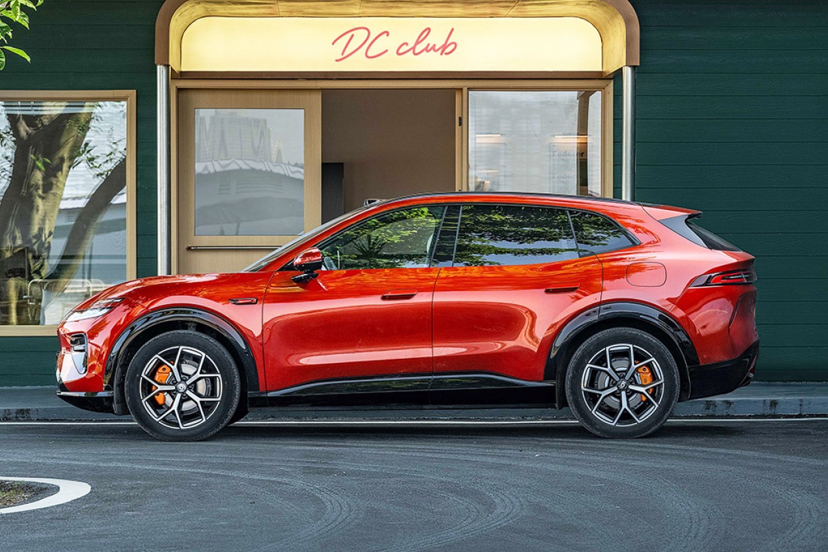 SUV vermelho brilhante estacionado de perfil em frente a um prédio verde escuro com uma placa iluminada DC club acima da porta
