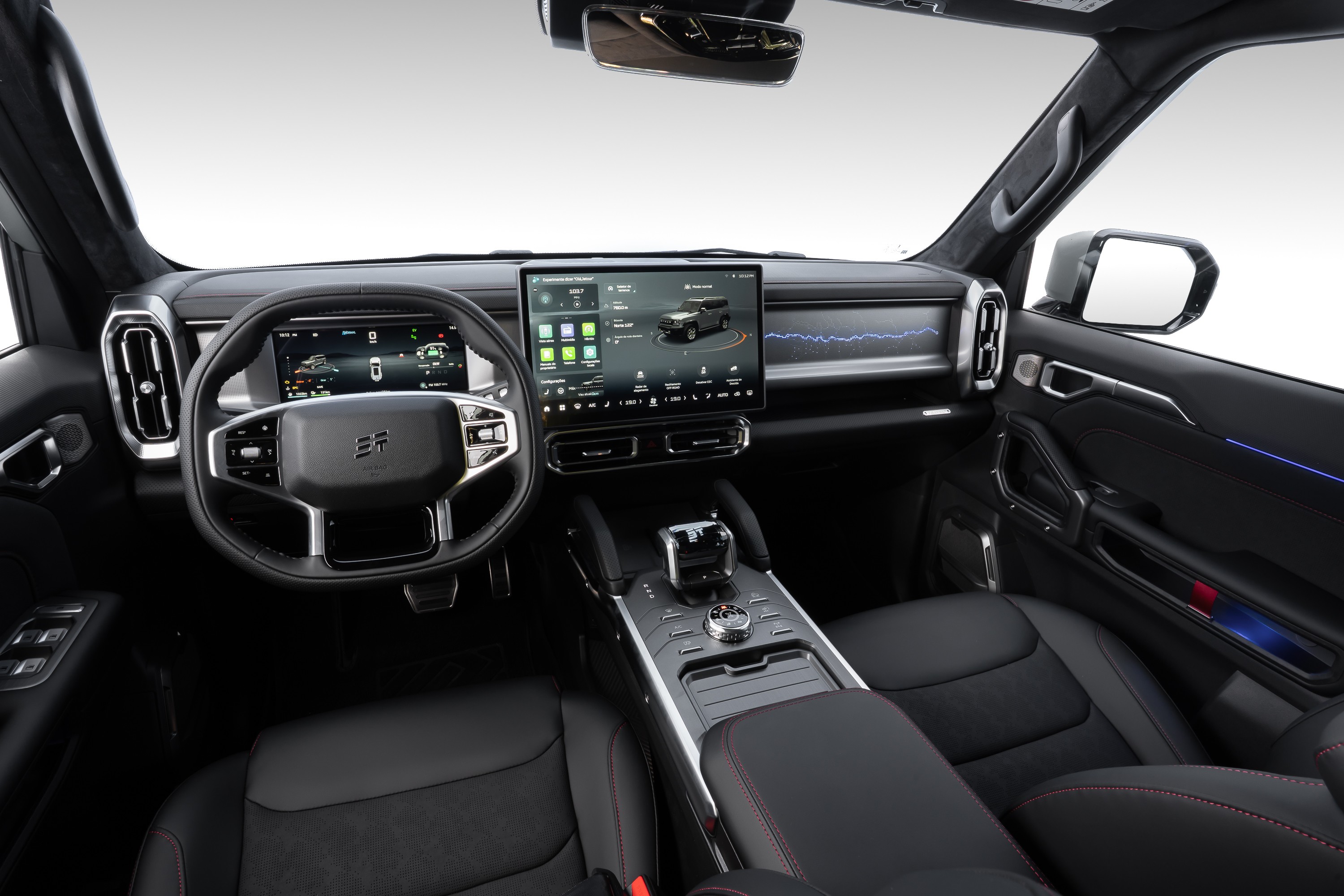 Interior de um carro moderno, com volante multifuncional e duas telas digitais grandes no painel. A tela central exibe um SUV cinza e ícones de aplicativos. O console central tem um seletor de marcha e botões giratórios. Os bancos são pretos com costura vermelha, e há detalhes em azul na porta do passageiro e no painel. O ambiente é escuro e tecnológico