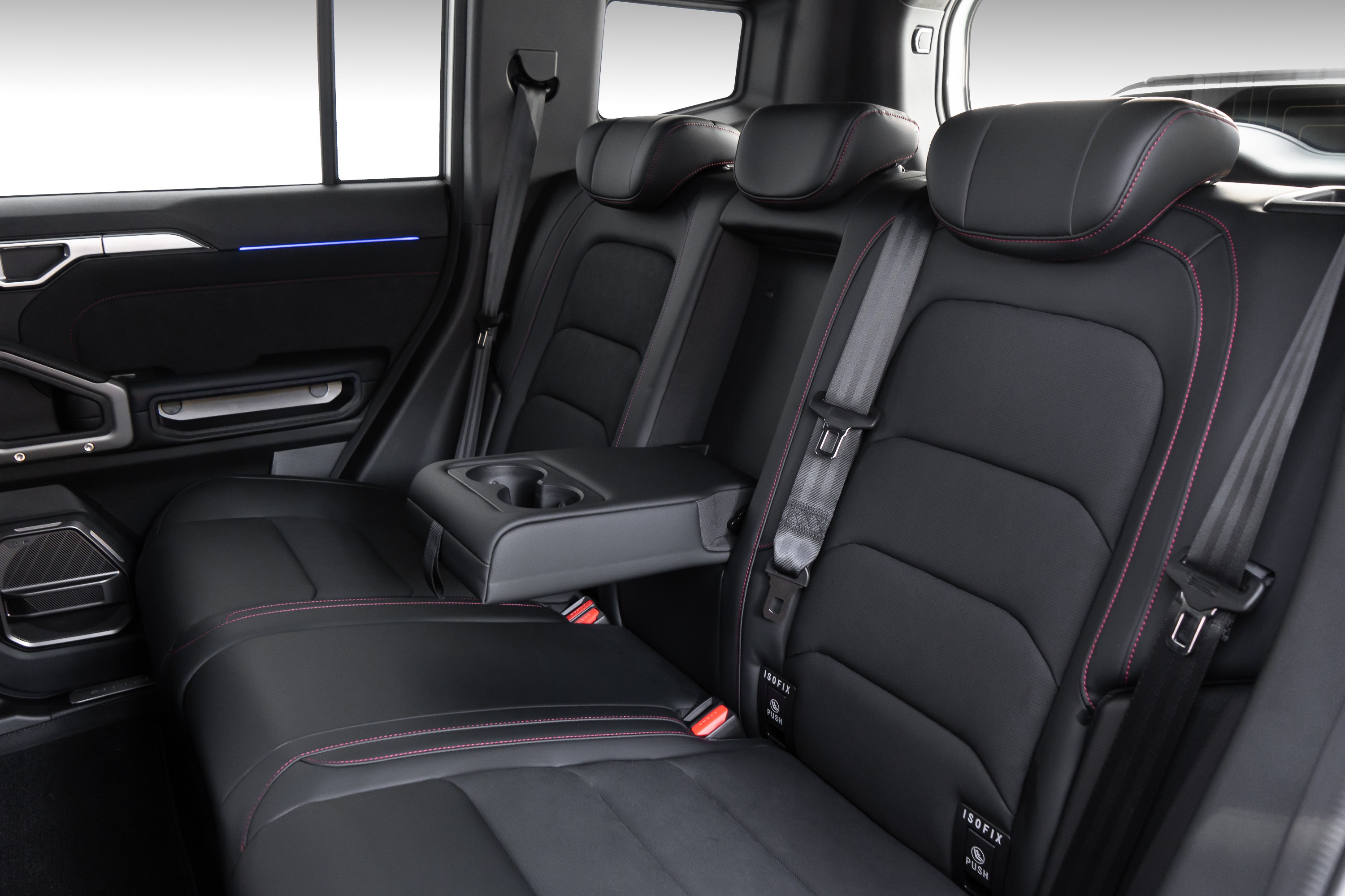 Interior de carro com bancos traseiros de couro preto e costura vermelha, cinto de segurança e apoio de braço central rebatido com porta-copos. Detalhe de luz ambiente azul na porta.
