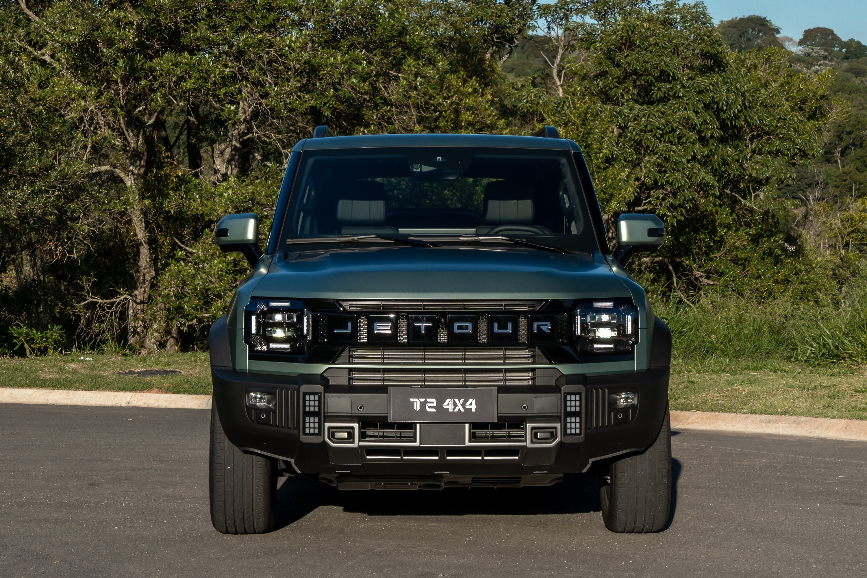 SUV Jetour T2 4x4 verde escuro, visto de frente, parado em asfalto com árvores e grama ao fundo