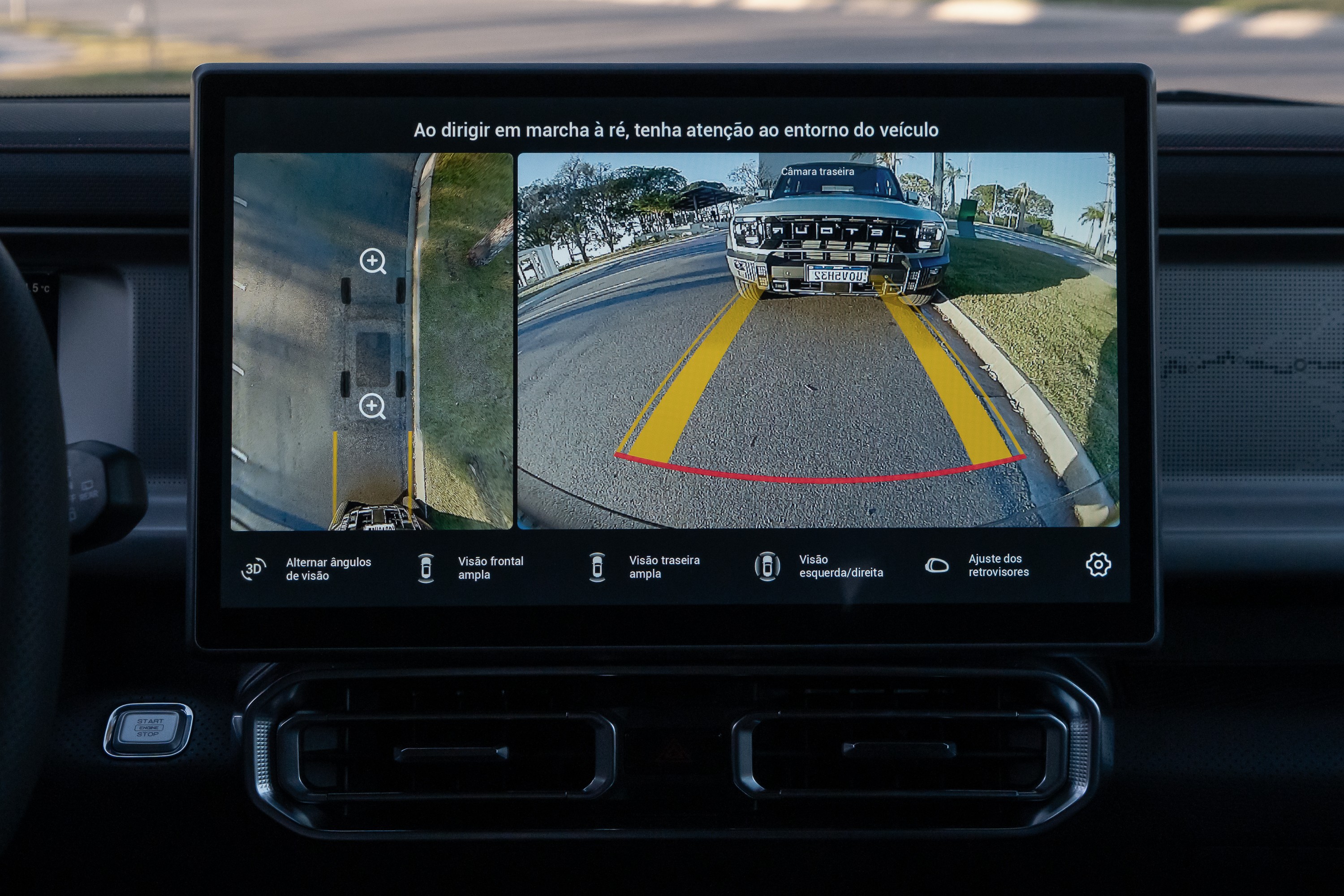 Tela multimídia de carro exibindo três câmeras: visão superior do veículo, visão traseira com linhas de guia amarelas e vermelhas, e visão frontal de outro carro. Há opções de visualização e ajuste de retrovisores na parte inferior da tela