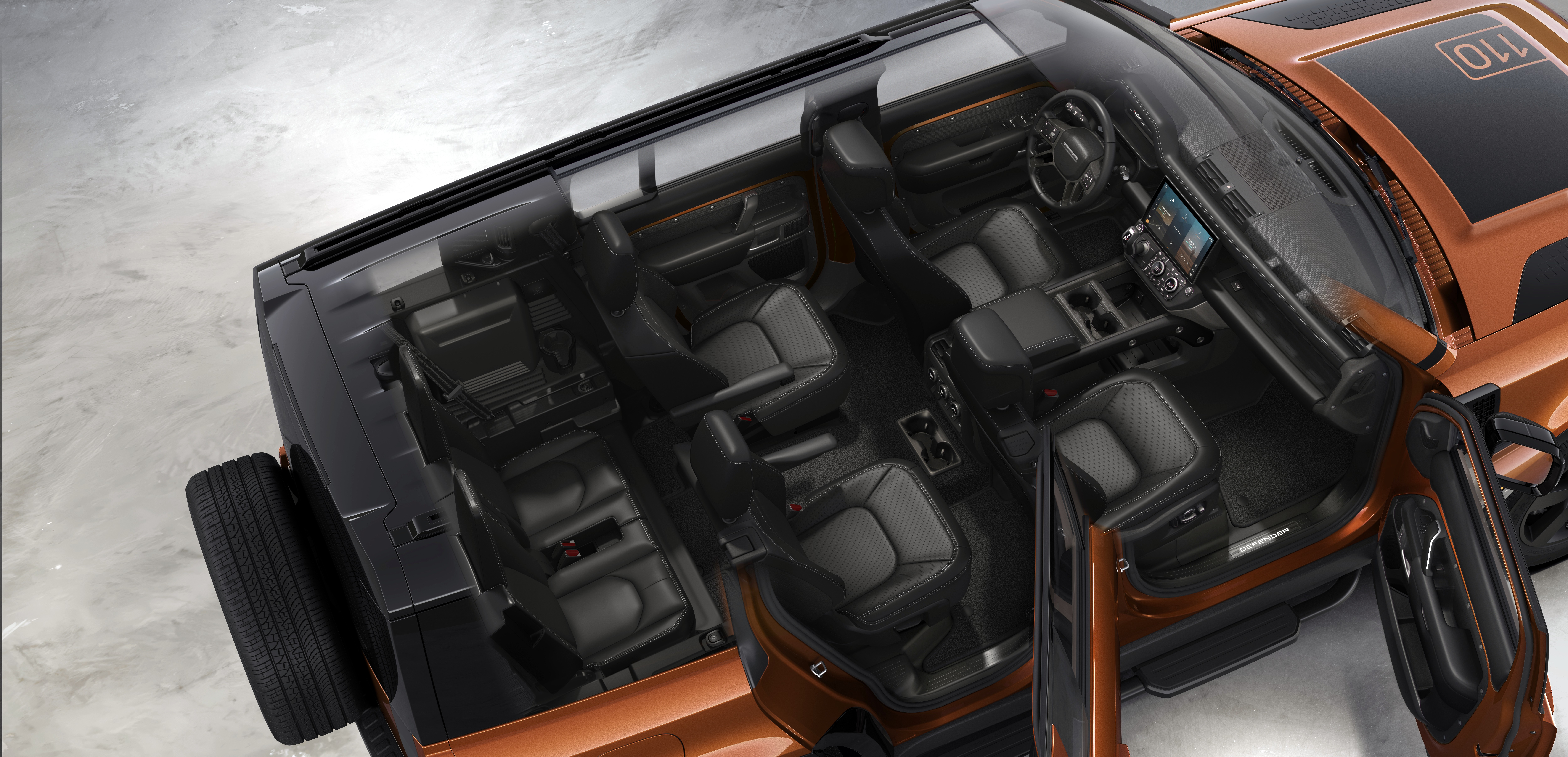 Vista aérea do interior de um carro SUV laranja com teto preto, mostrando os bancos de couro escuro e o painel com tela digital. A porta do passageiro está aberta, revelando o espaço interno e o pneu sobressalente na traseira.