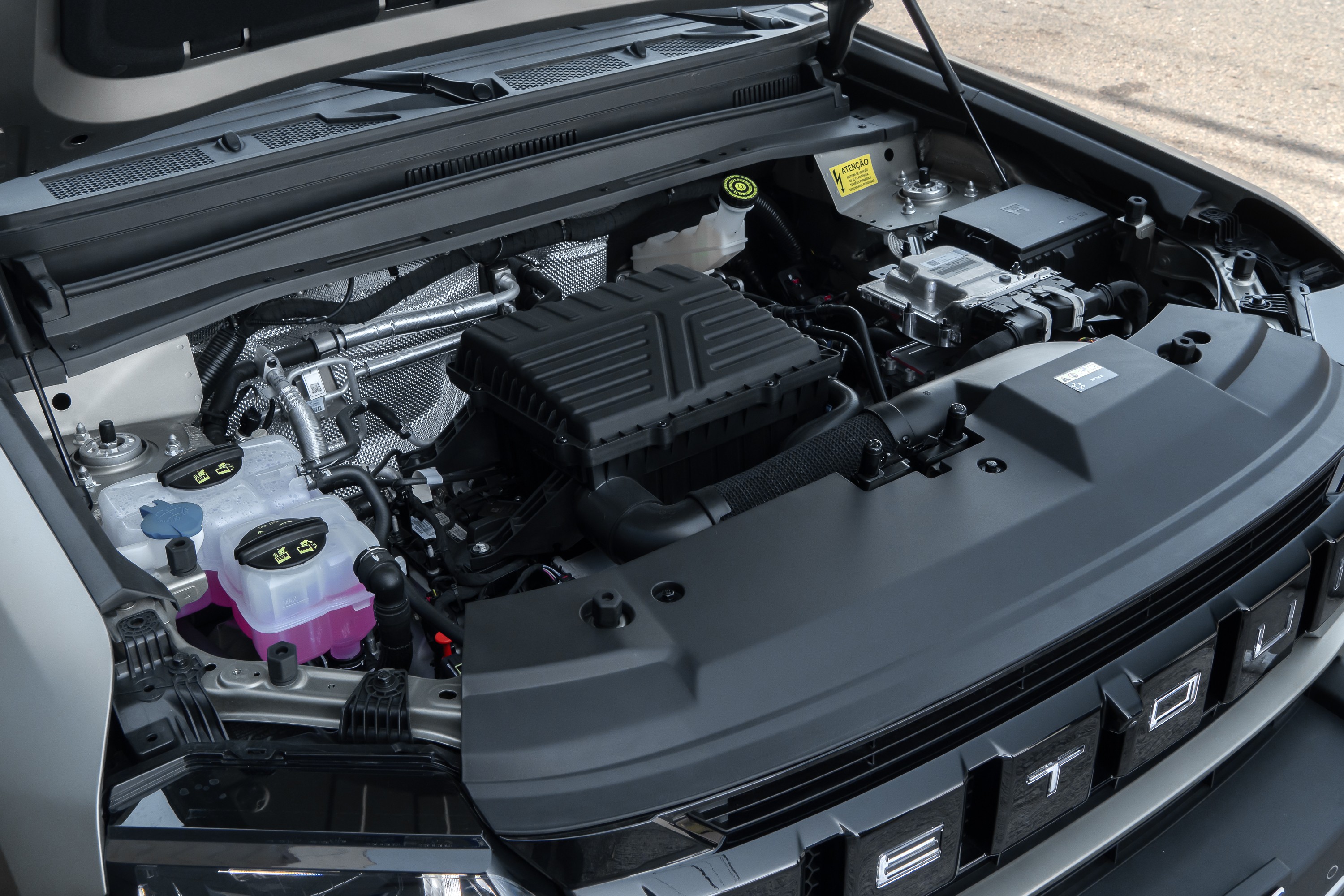 Motor de carro moderno com capô aberto, mostrando componentes como filtro de ar preto, reservatórios de fluidos transparentes com líquidos coloridos e fiação organizada