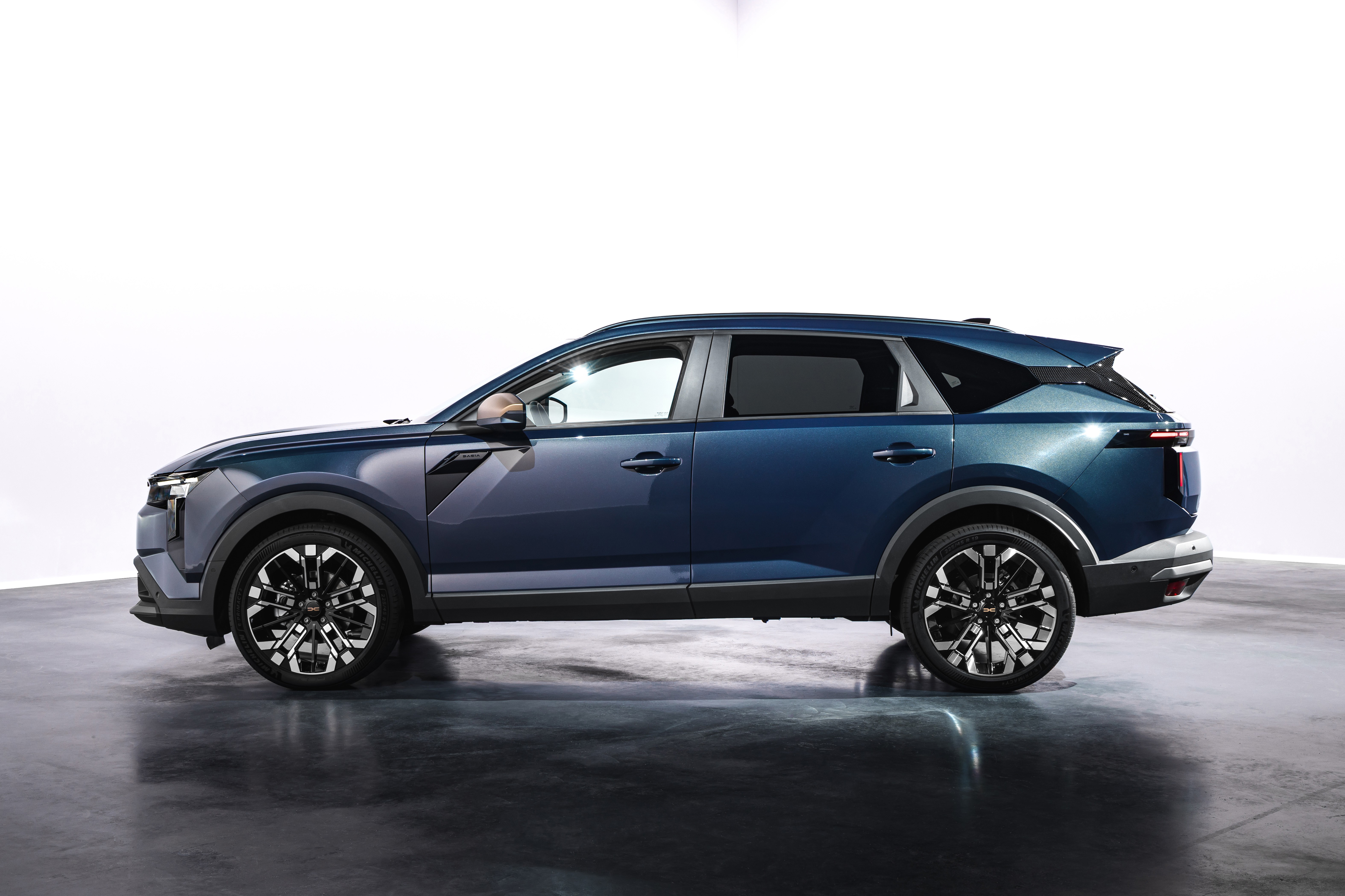 SUV azul escuro, com detalhes pretos nas caixas de roda e para-choques, visto de perfil em um estúdio com fundo branco e chão escuro reflexivo