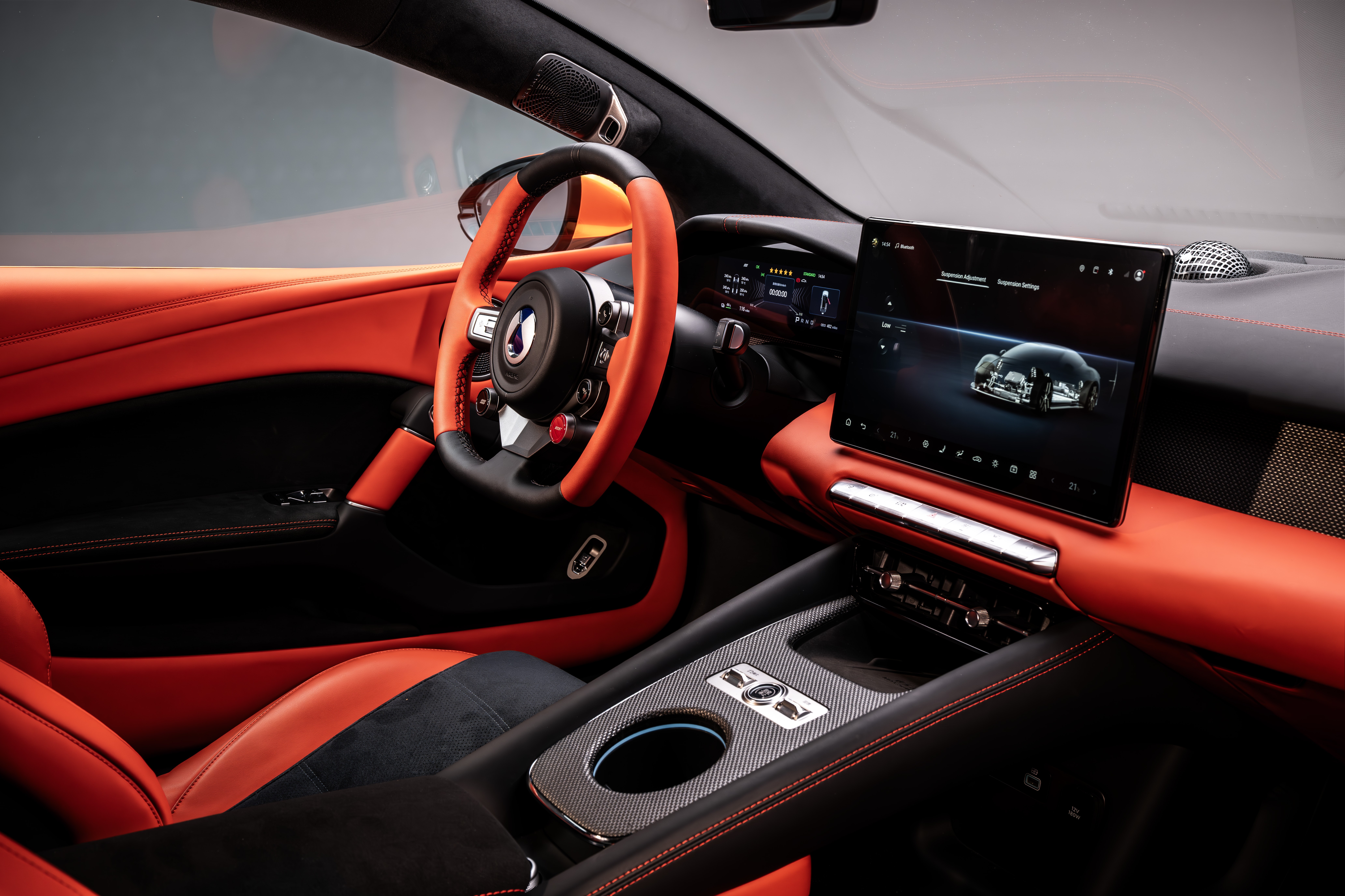 Interior de carro esportivo com estofamento laranja e preto, volante laranja e tela multimídia exibindo um carro prateado