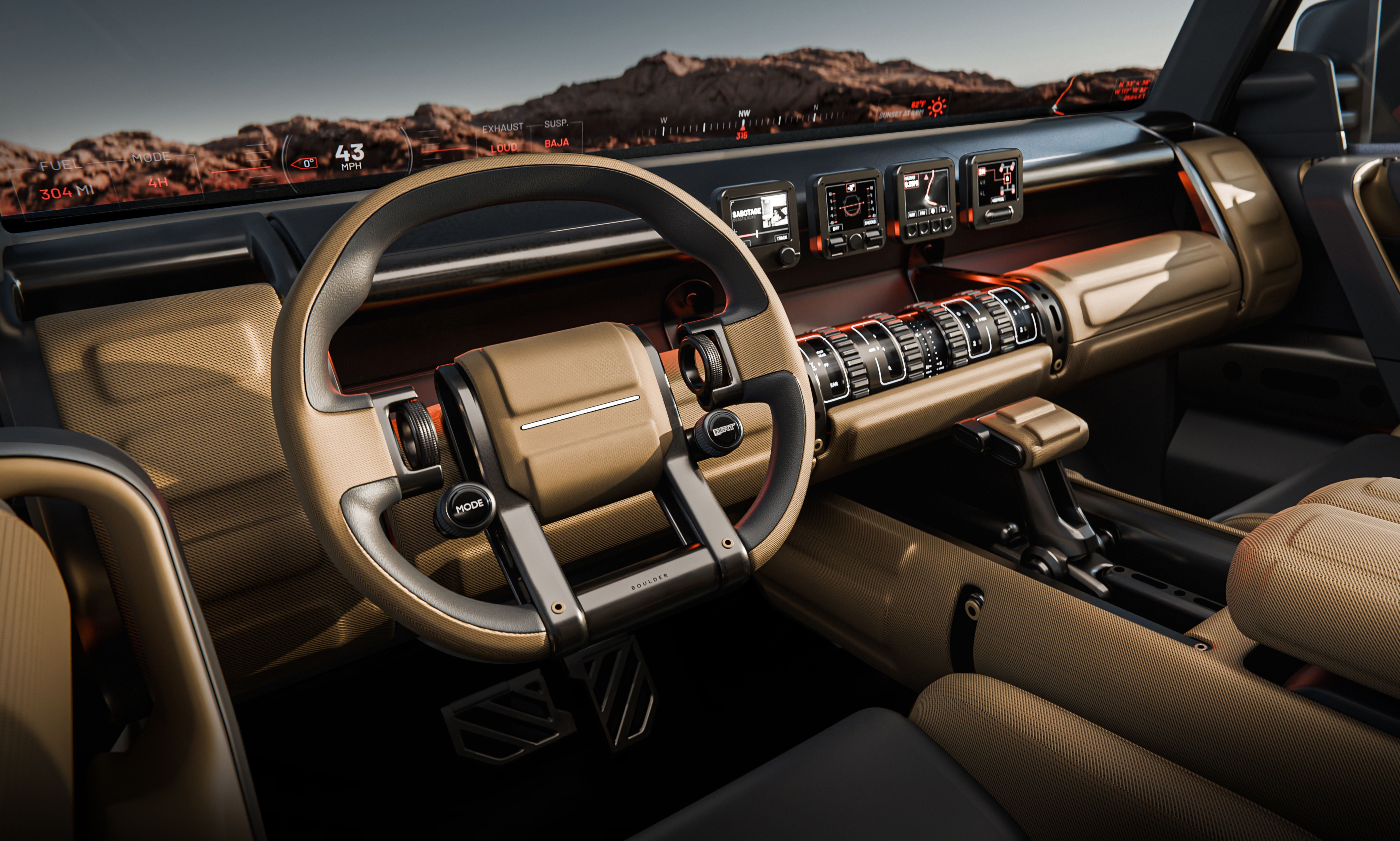 Interior de um carro moderno com volante bege e cinza, painel com telas digitais e botões rotativos, e bancos bege. Ao fundo, montanhas rochosas sob um céu claro.