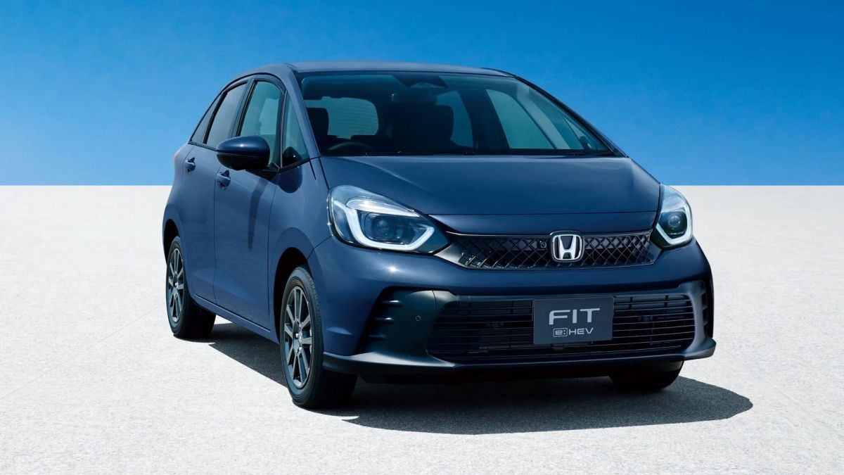 Carro azul-marinho Honda Fit e:HEV, modelo hatch, parado em uma superfície branca com céu azul claro ao fundo