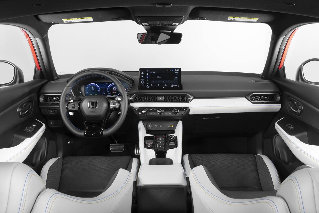 Interior de um carro moderno, com painel preto e detalhes brancos. O volante escuro tem o logotipo Honda. À esquerda, o painel de instrumentos digital exibe informações em azul. No centro, uma tela multimídia sensível ao toque. Os bancos dianteiros são pretos com laterais brancas e costura azul