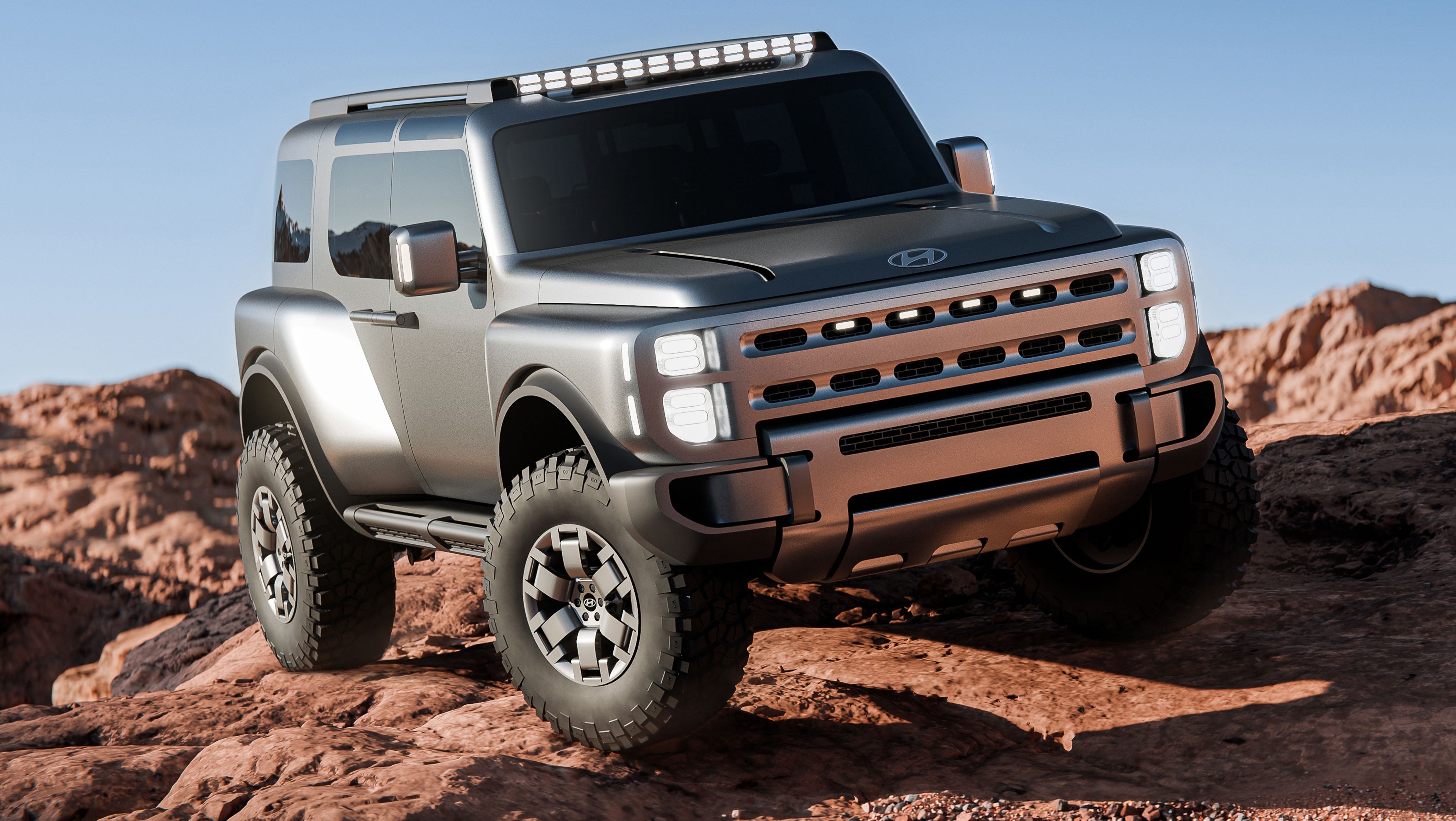 Jipe Hyundai conceito cinza-chumbo com faróis quadrados acesos, grade robusta e pneus off-road, parado em terreno rochoso marrom sob céu azul claro