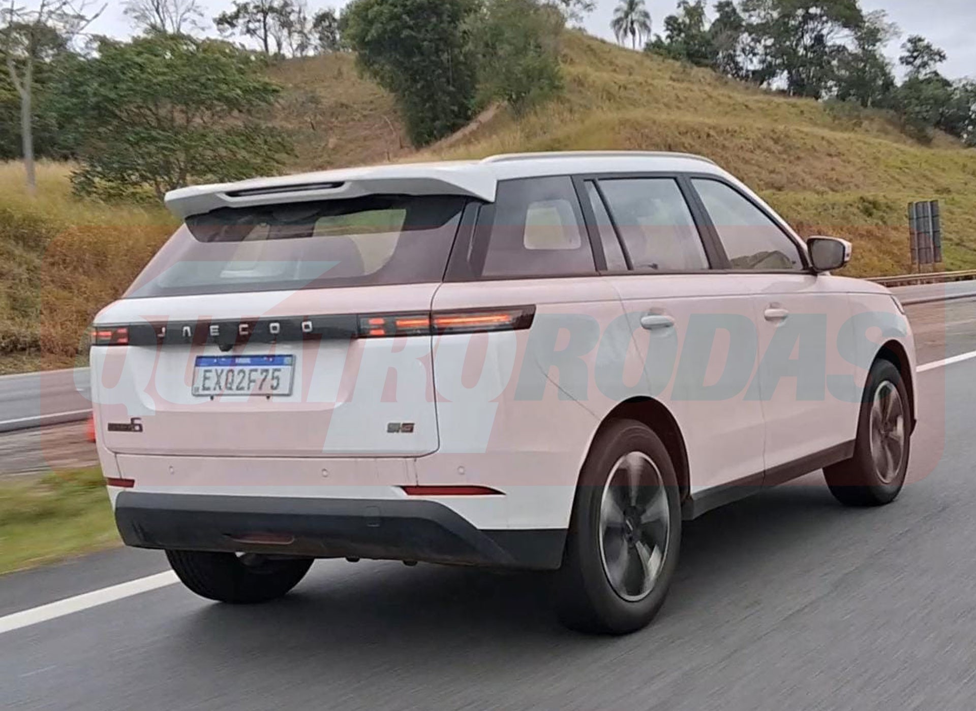 SUV branco Jaecoo J6 com placa brasileira EXQ2F75, visto de traseira e lateral, trafegando em rodovia com vegetação ao fundo
