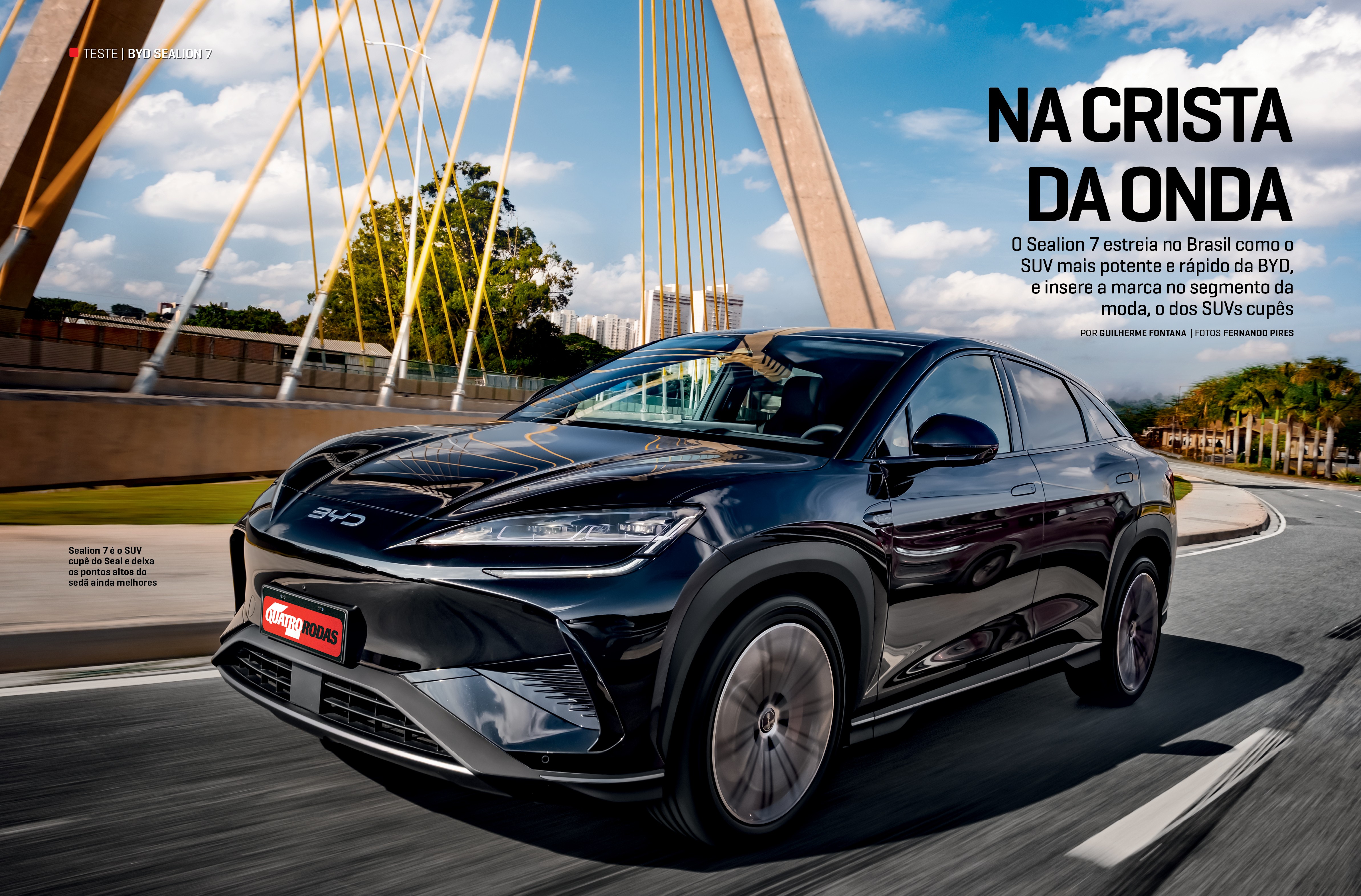 Um SUV cupê preto brilhante, o BYD Sealion 7, em movimento numa estrada, com o logotipo BYD no capô. Ao fundo, um céu azul com nuvens brancas e a estrutura de um viaduto estaiado com cabos amarelos. À direita, árvores e edifícios distantes. A imagem transmite velocidade e modernidade