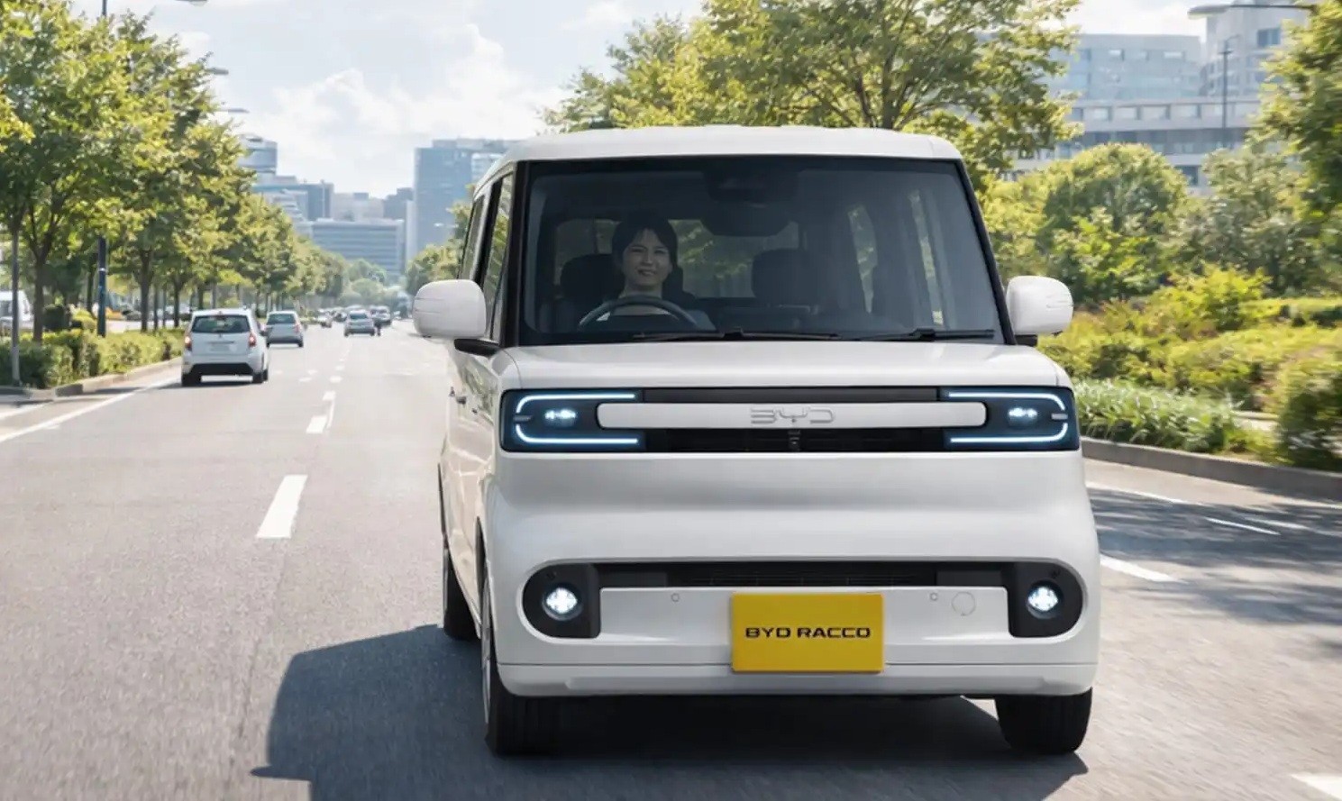 Carro elétrico BYD Racco branco, compacto e quadrado, com uma mulher sorrindo ao volante, trafegando em uma avenida arborizada com outros veículos ao fundo