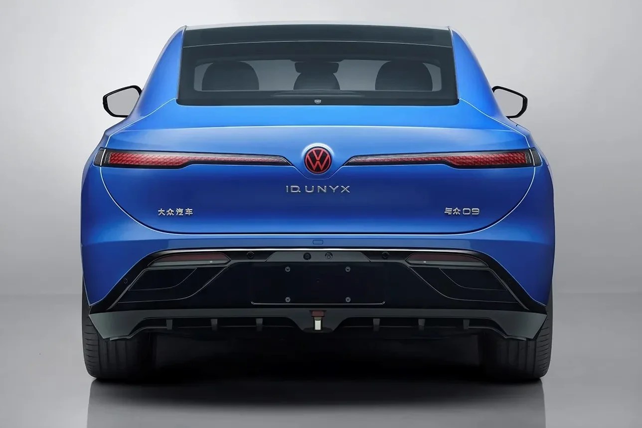 Traseira de um carro azul-elétrico, modelo Volkswagen ID.UNYX, com lanternas horizontais vermelhas e logotipo VW em vermelho. O para-choque inferior é preto, com detalhes aerodinâmicos e sensores de estacionamento. O vidro traseiro é escuro, e o carro está centralizado em um fundo cinza claro