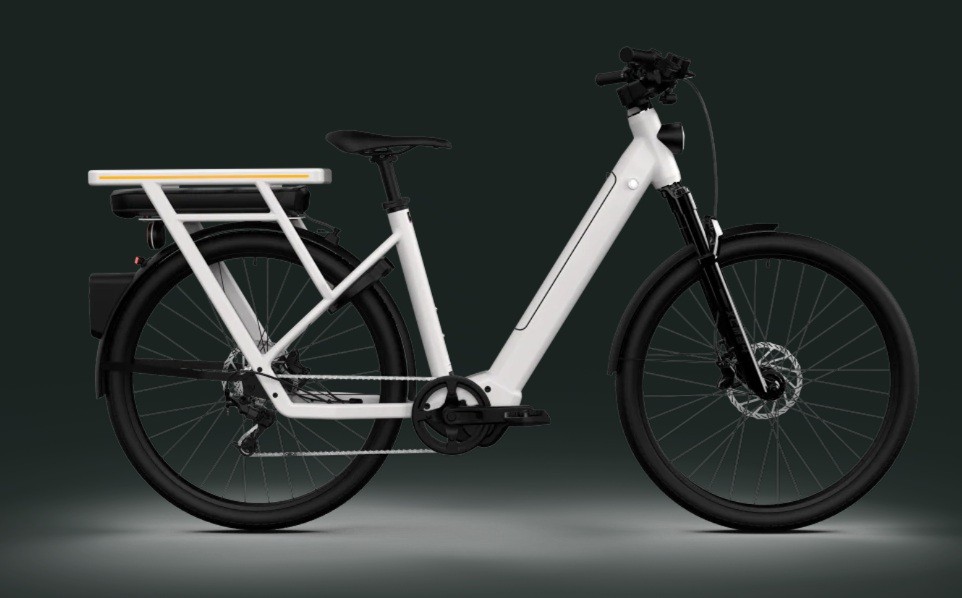 Bicicleta elétrica branca com quadro moderno, bateria preta no bagageiro traseiro e luz amarela. Possui pneus pretos, para-lamas e freios a disco, em fundo cinza escuro