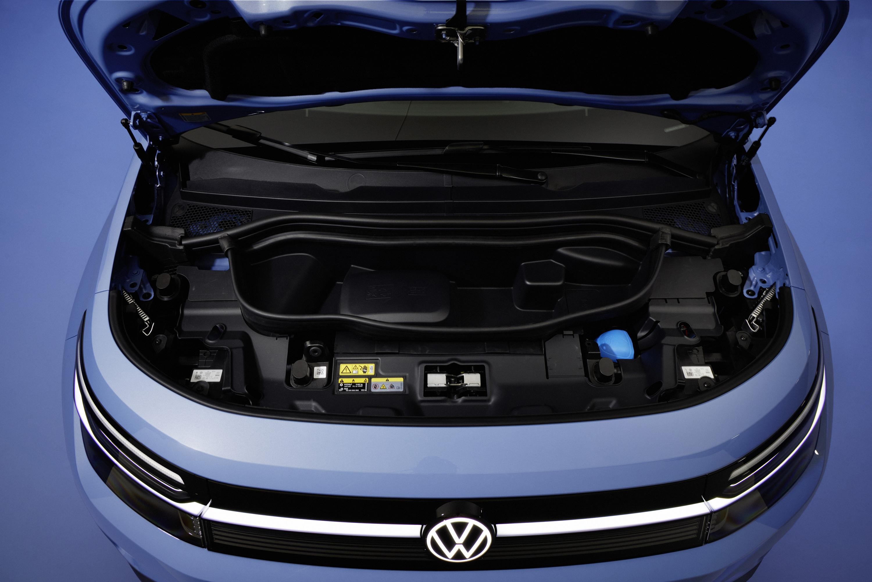 Capô azul de um carro elétrico Volkswagen aberto, revelando um compartimento de armazenamento frontal vazio, com o logotipo da marca iluminado na grade inferior