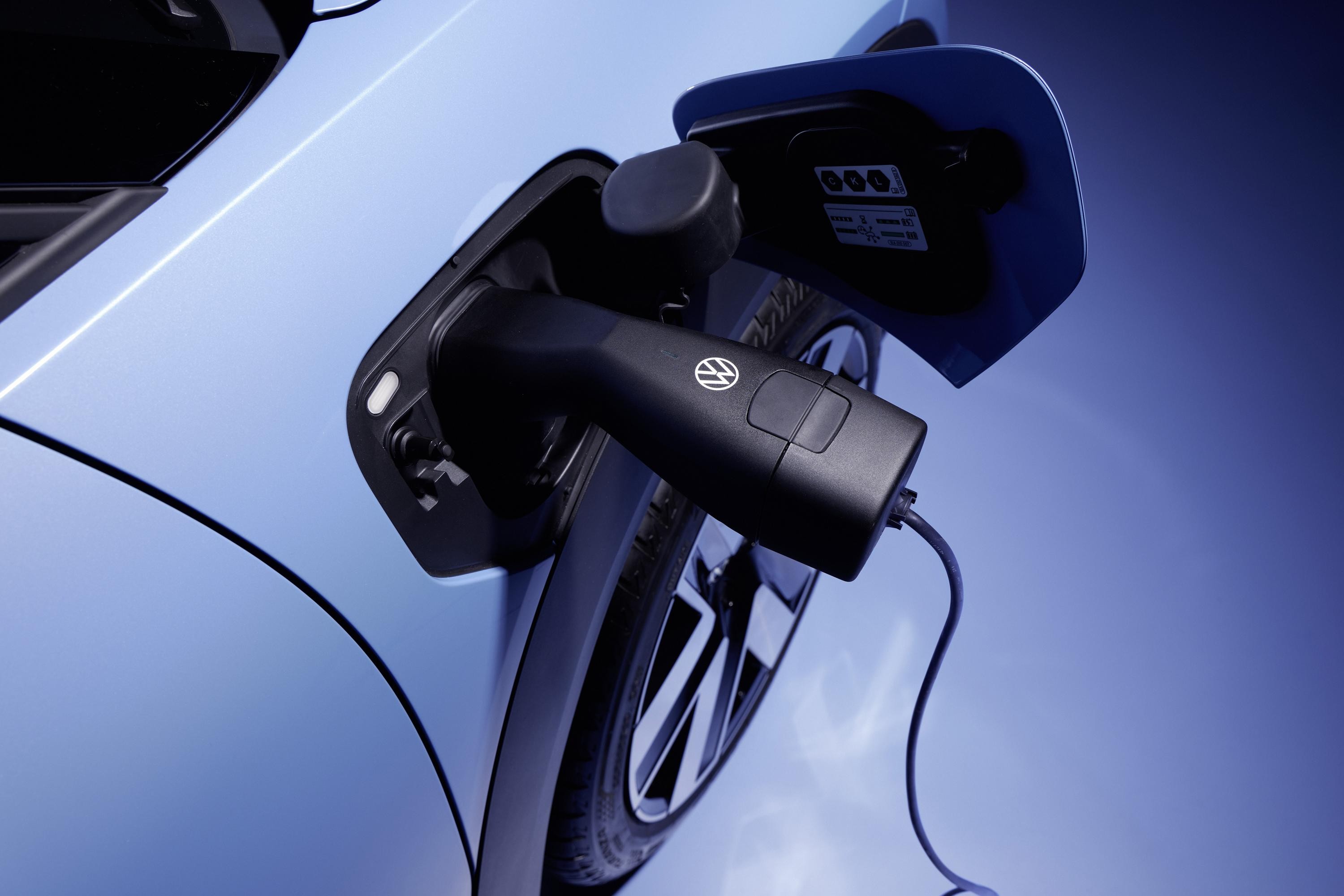 Carregador preto com logo Volkswagen conectado à entrada de um carro elétrico azul, com a tampa aberta e o cabo esticado