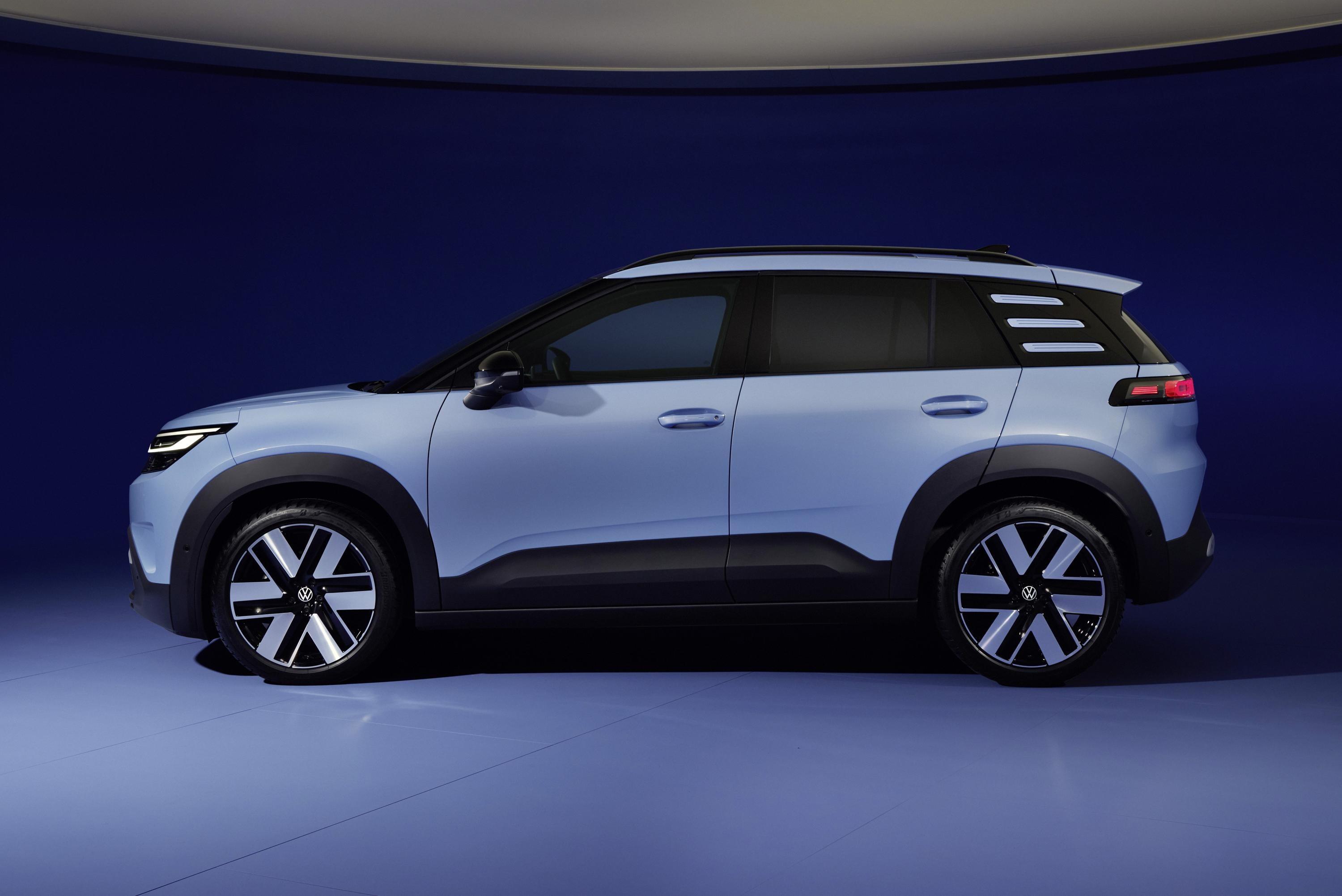 SUV compacto azul claro, visto de perfil, com detalhes em preto fosco nas caixas de roda e na parte inferior da carroceria. As rodas têm design moderno em preto e prata, e o carro está em um estúdio com fundo azul escuro e piso azul claro.