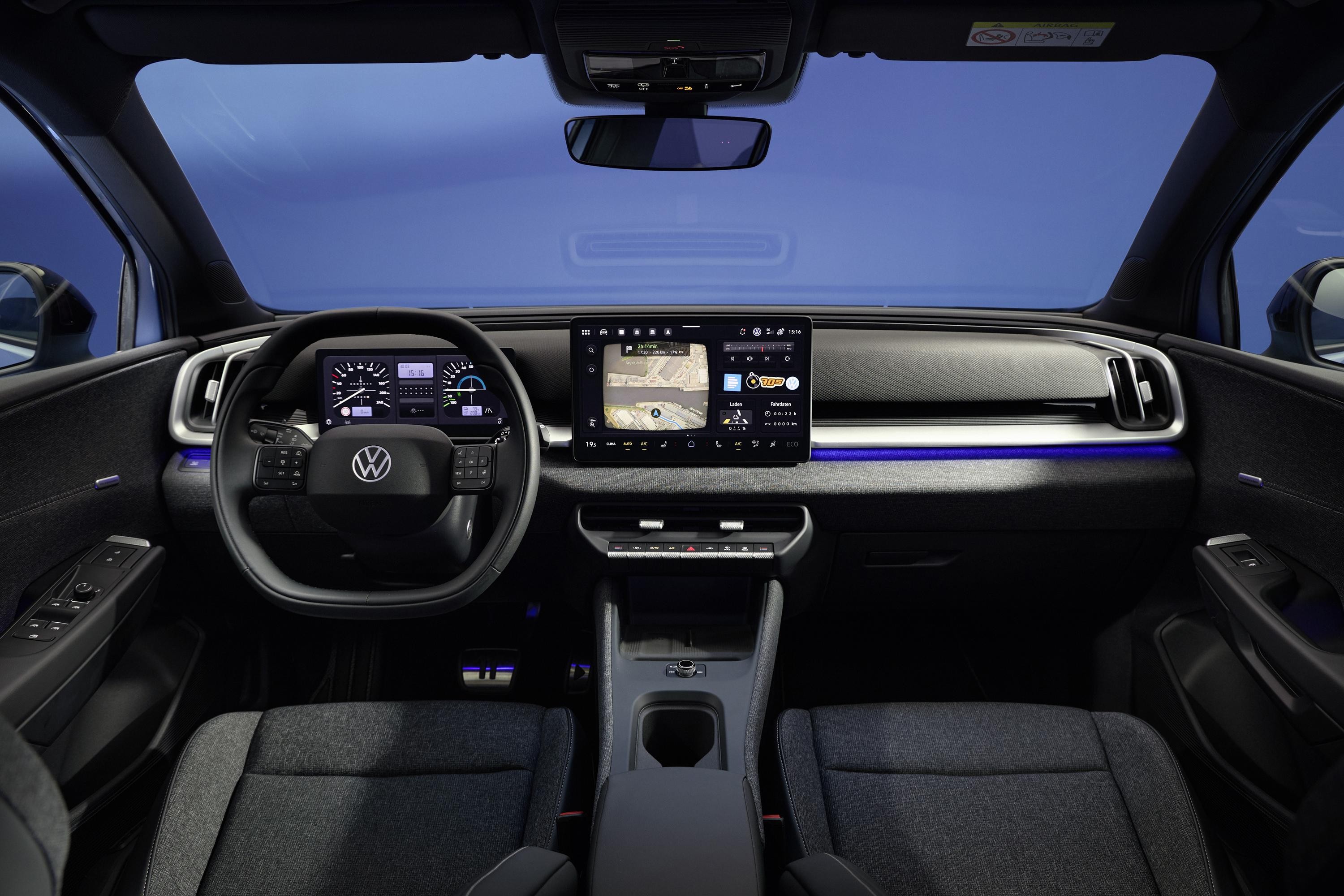 Interior de um carro moderno com volante preto, painel digital e tela multimídia central exibindo um mapa. Há uma faixa de luz azul no painel e bancos de tecido escuro. O para-brisa mostra um céu azul
