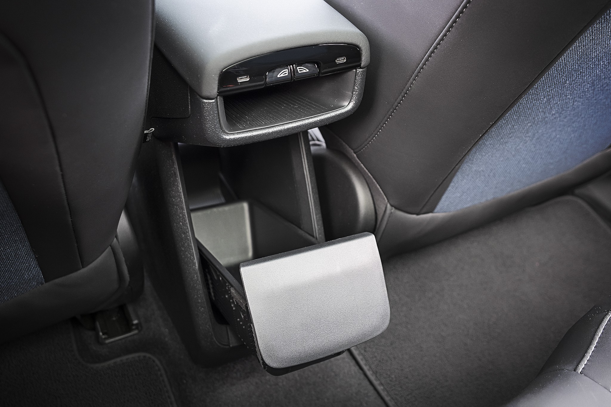 Interior de carro, mostrando o console central traseiro com porta-objetos aberto e botões para vidros elétricos. Os bancos são cinza escuro com detalhes em tecido azul. O carpete é cinza.