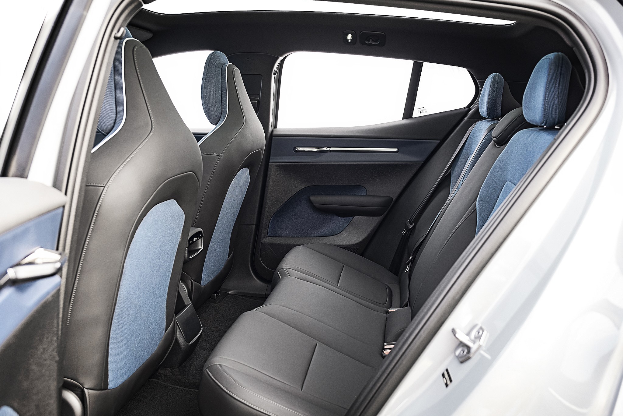 Interior de um carro com bancos de couro preto e detalhes em tecido azul claro. Os bancos dianteiros têm encostos altos e os traseiros são um banco corrido para três pessoas. As portas têm acabamento em azul escuro e detalhes cromados. As janelas estão abertas, mostrando um fundo branco
