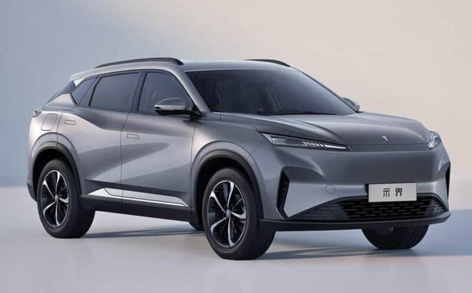 SUV elétrico cinza-chumbo, com design moderno e linhas fluidas, visto de frente e lateralmente. Possui faróis finos, grade frontal fechada e rodas de liga leve com detalhes pretos e prateados. Um emblema chinês está na placa dianteira