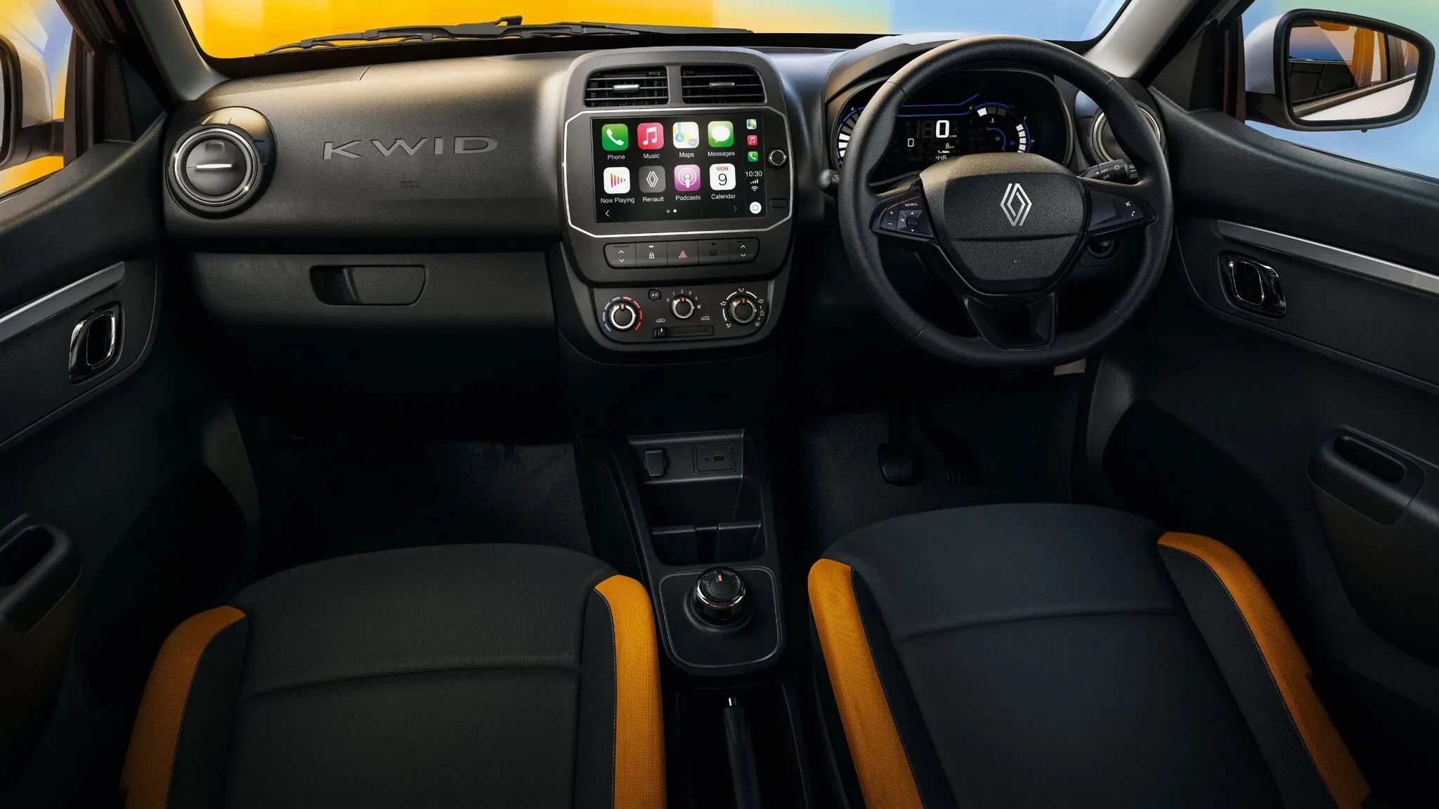Interior de um carro Renault Kwid, com painel preto e detalhes em laranja nos bancos. O volante tem o logo da Renault, e o painel central exibe uma tela multimídia com aplicativos de celular. O nome KWID está em relevo no painel do lado do passageiro
