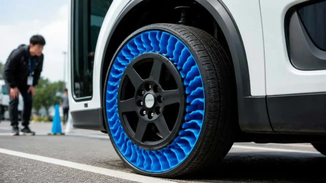 Pneu sem ar com estrutura interna azul vibrante em um carro branco, com um homem asiático de jaqueta preta observando ao fundo