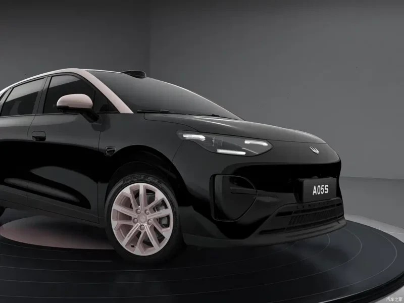 Carro elétrico preto com teto e retrovisores brancos, rodas prateadas, exibido em uma plataforma giratória preta em estúdio cinza