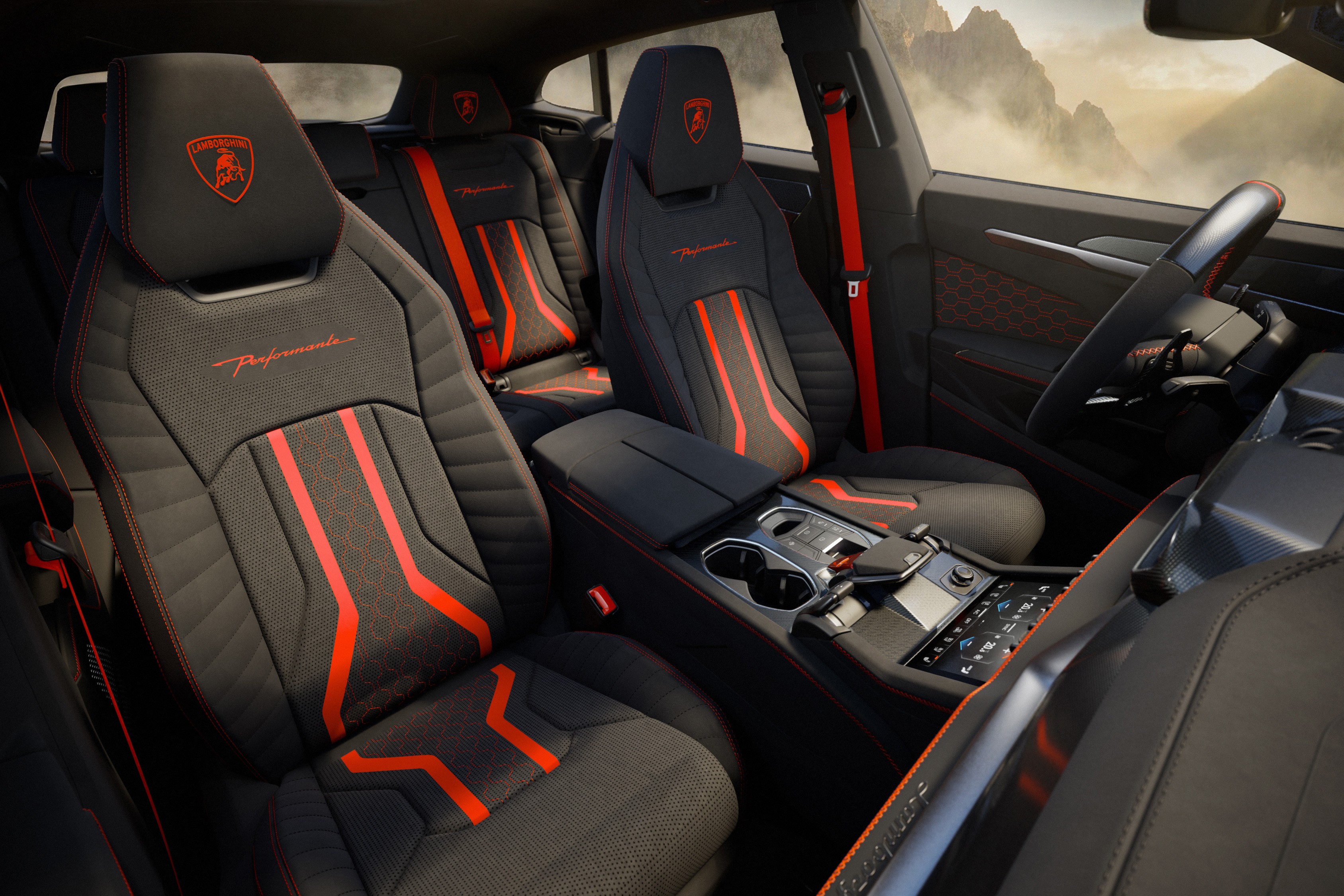 Interior de carro esportivo com bancos pretos e detalhes em vermelho, incluindo o logo da Lamborghini nos encostos de cabeça. O cinto de segurança é vermelho, e o painel central possui porta-copos e controles digitais. Ao fundo, montanhas nebulosas são visíveis pela janela