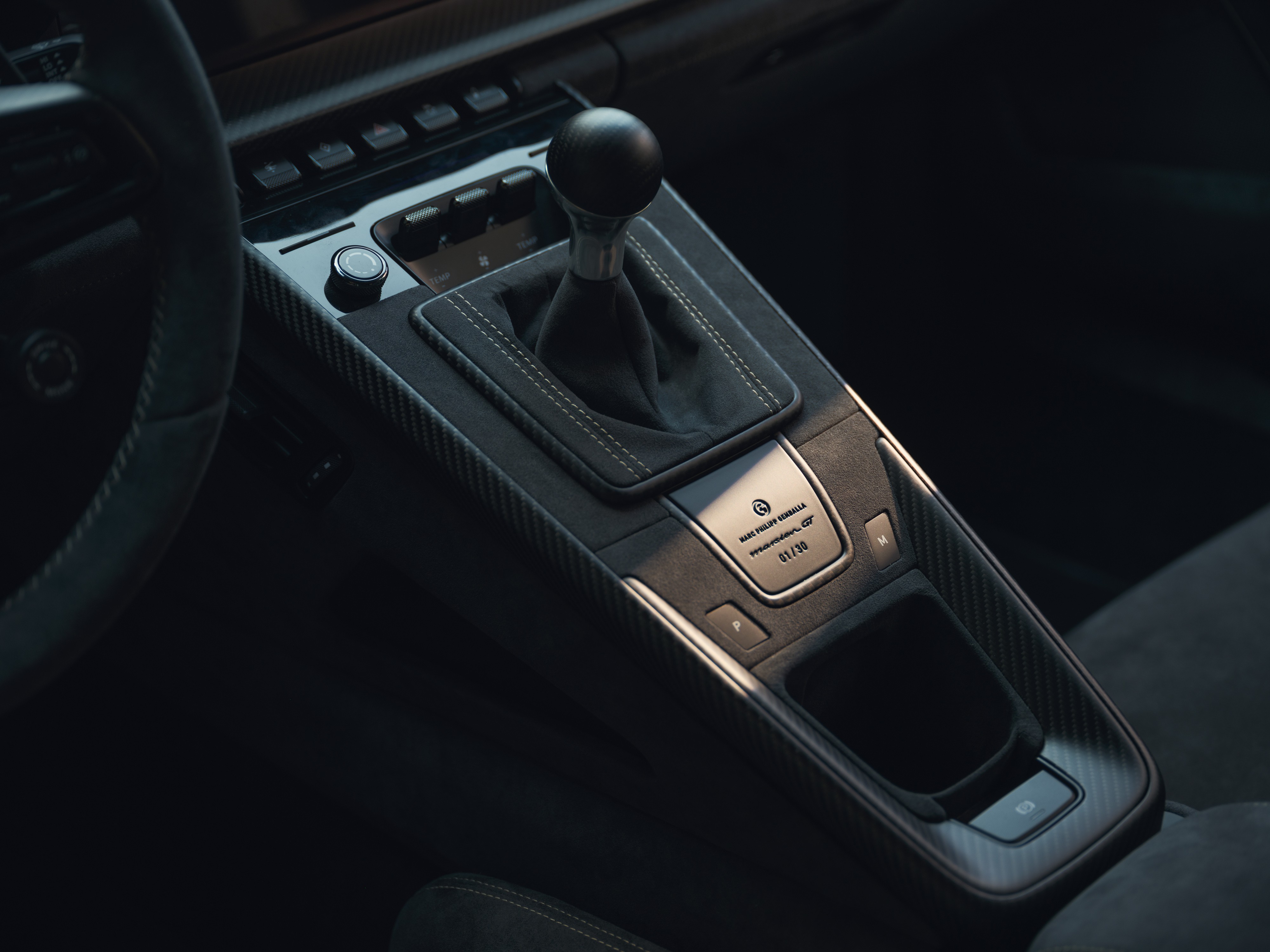 Interior de carro esportivo com console central em fibra de carbono e camurça escura, destacando o câmbio manual e uma placa metálica com a inscrição 01/10