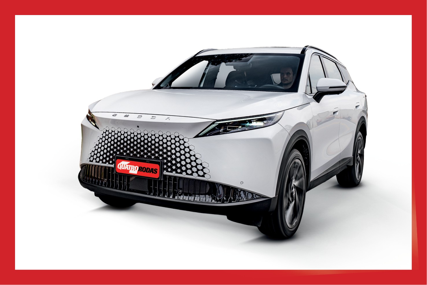 SUV branco moderno com grade frontal em padrão de colmeia, faróis afilados e placa QUATRO RODAS vermelha. Um motorista está visível no interior do veículo. O carro está em um fundo branco com borda vermelha