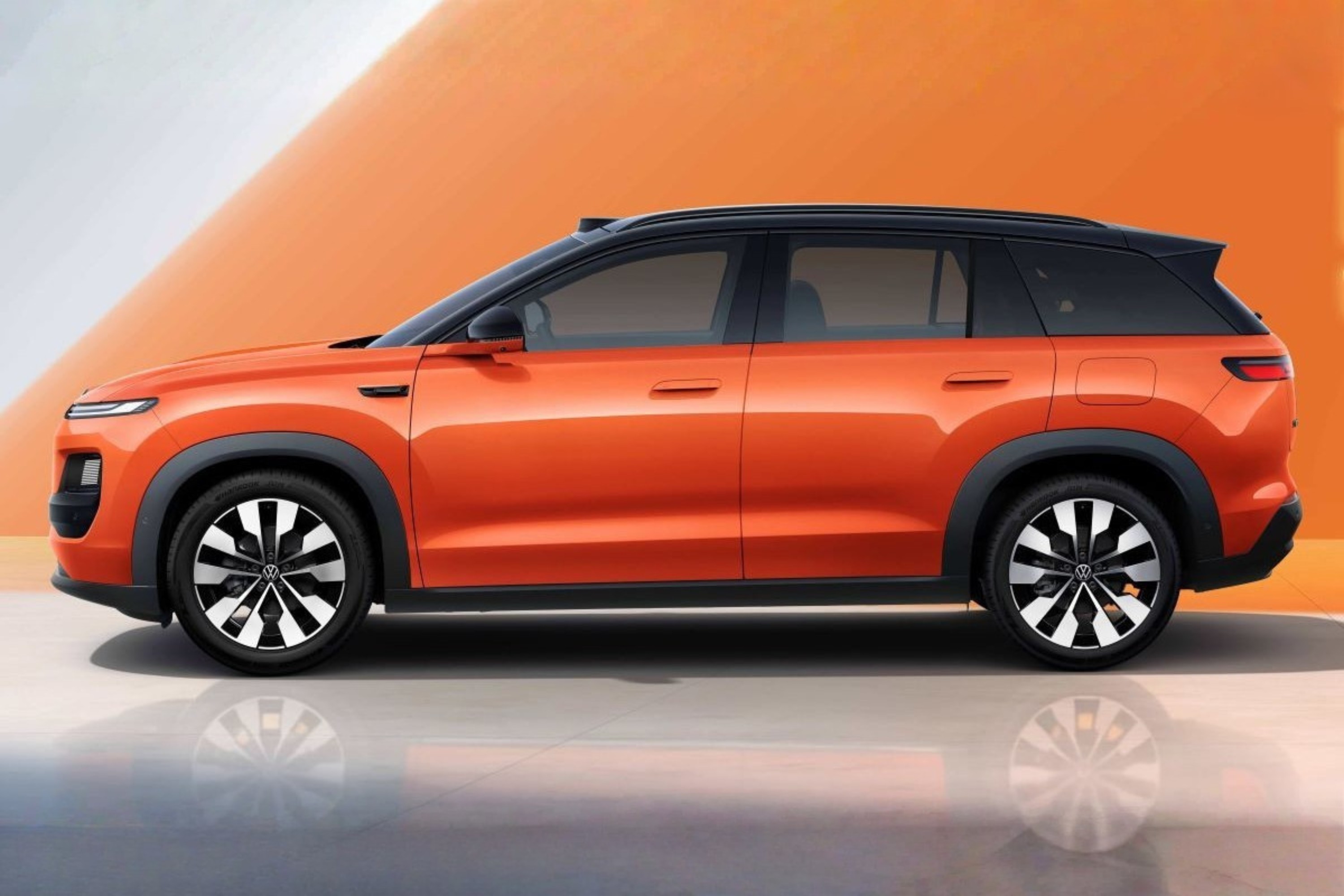 SUV laranja com teto preto, visto de perfil, parado sobre uma superfície cinza que reflete suas rodas. O fundo é laranja com uma faixa diagonal branca
