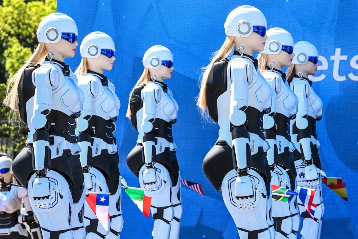 Robôs humanoides femininos, com cabelos loiros e óculos azuis, enfileirados em um evento, com bandeiras de países como Chile e Itália presas aos seus braços, em frente a um fundo azul