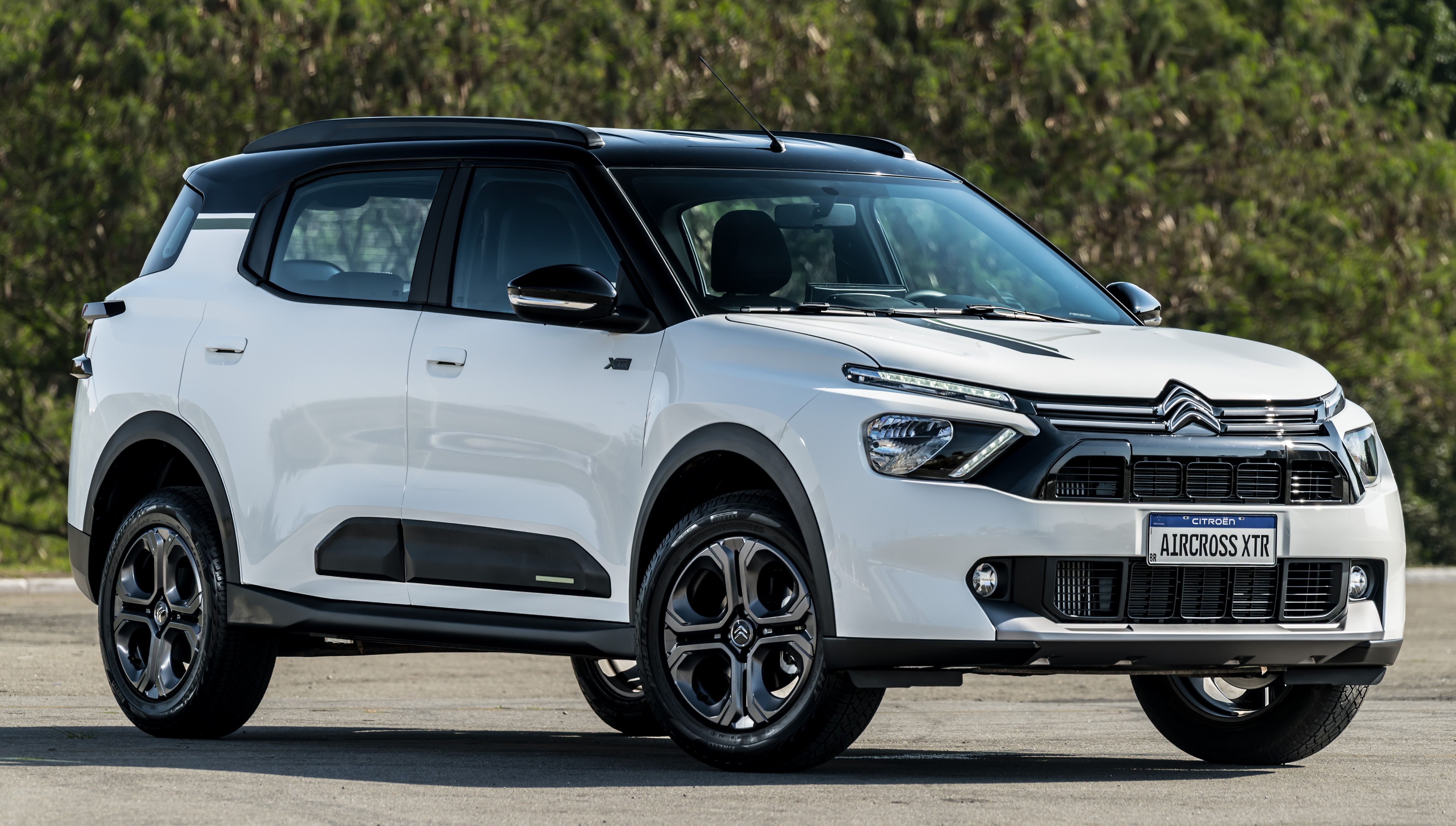 SUV Citroën Aircross XTR branco com teto preto, estacionado em uma rua asfaltada com árvores ao fundo