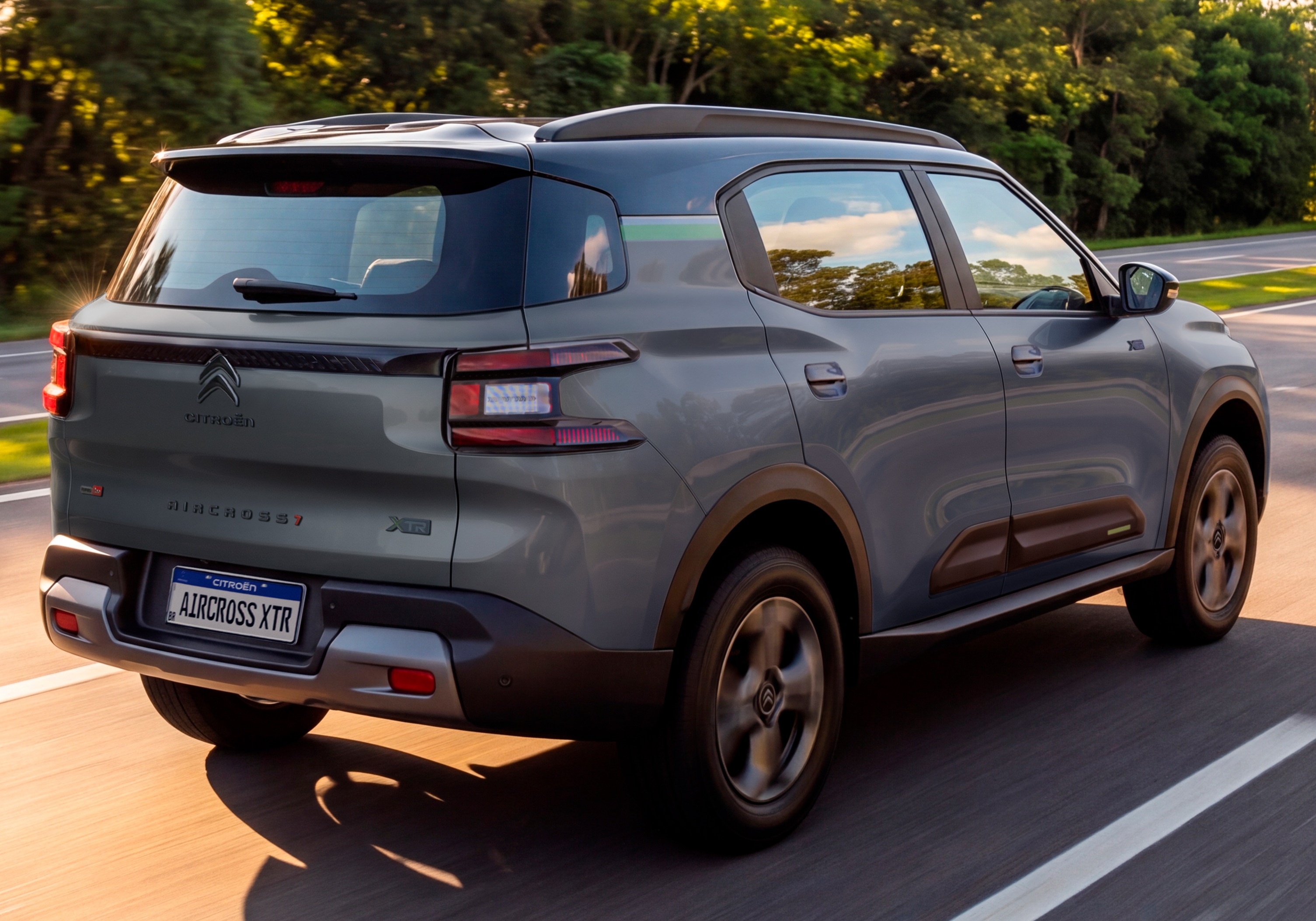 SUV Citroën Aircross XTR cinza escuro, visto de traseira e lateral, em movimento numa estrada asfaltada com árvores ao fundo