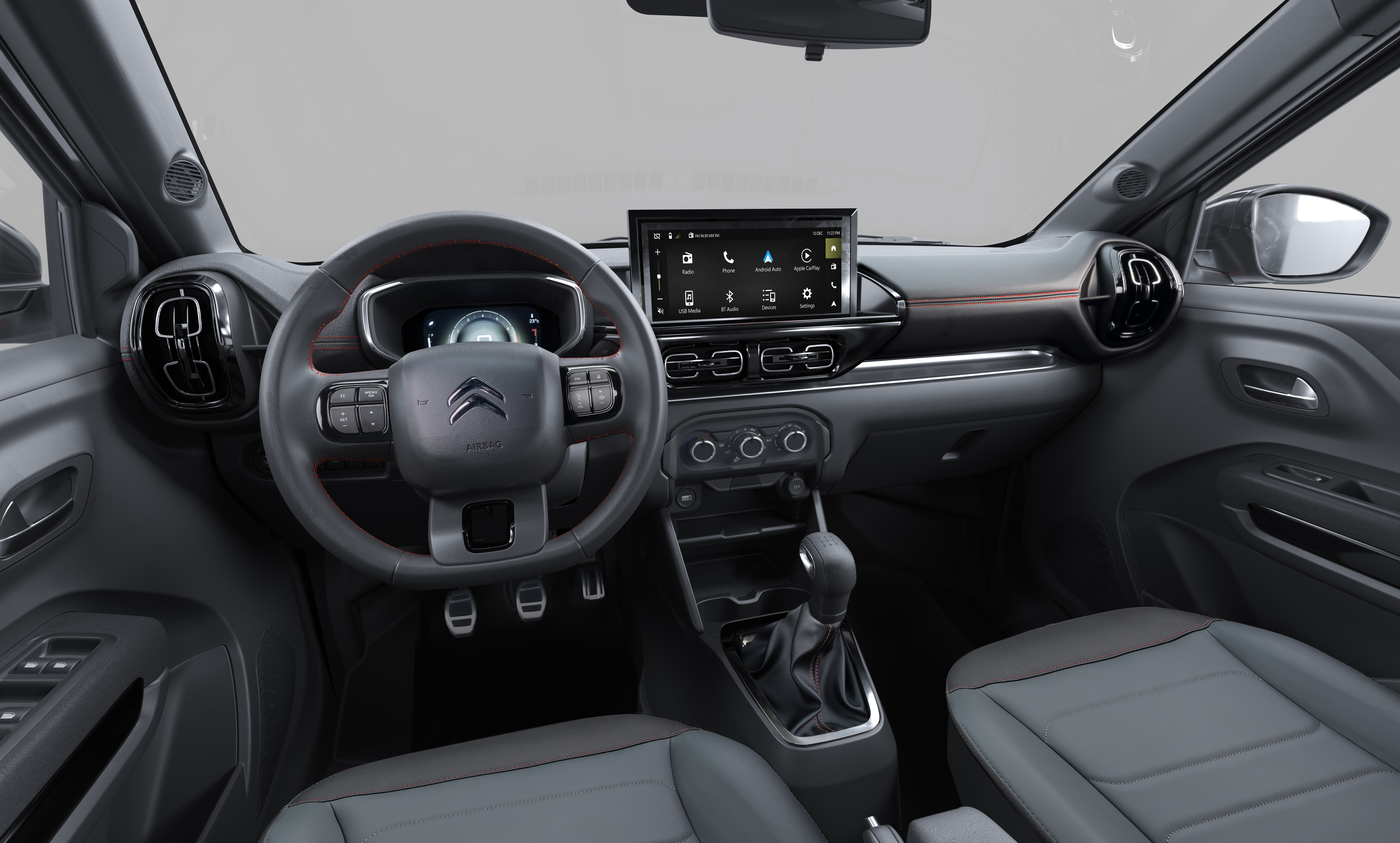Interior de um carro moderno com painel cinza escuro, volante multifuncional, tela multim&iacute;dia central com &iacute;cones de aplicativos e c&acirc;mbio manual. Detalhes em laranja no painel e bancos de tecido cinza escuro e claro.