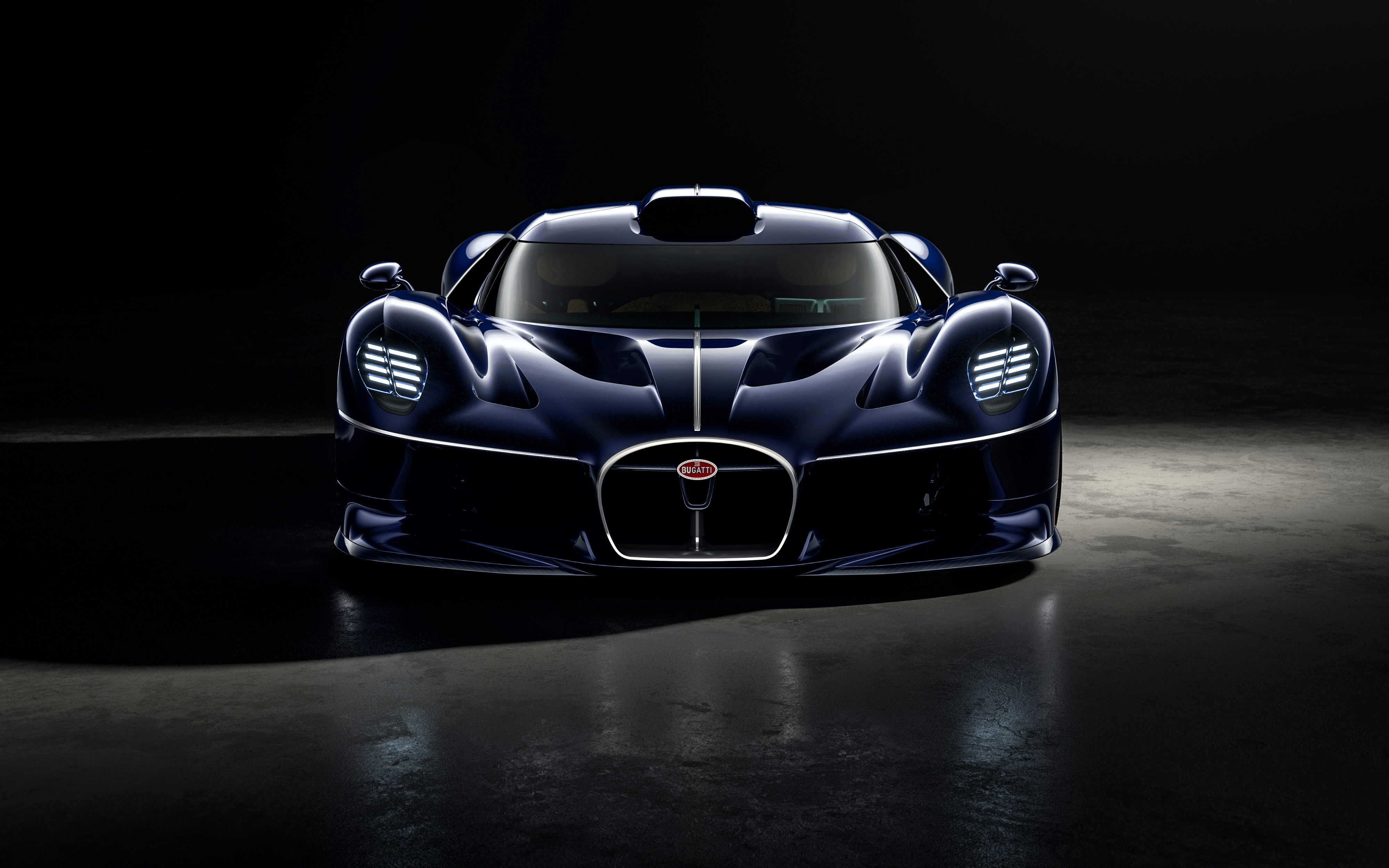 Carro esportivo Bugatti azul-marinho, visto de frente, com faróis acesos e grade frontal oval, em um ambiente escuro com reflexos no chão