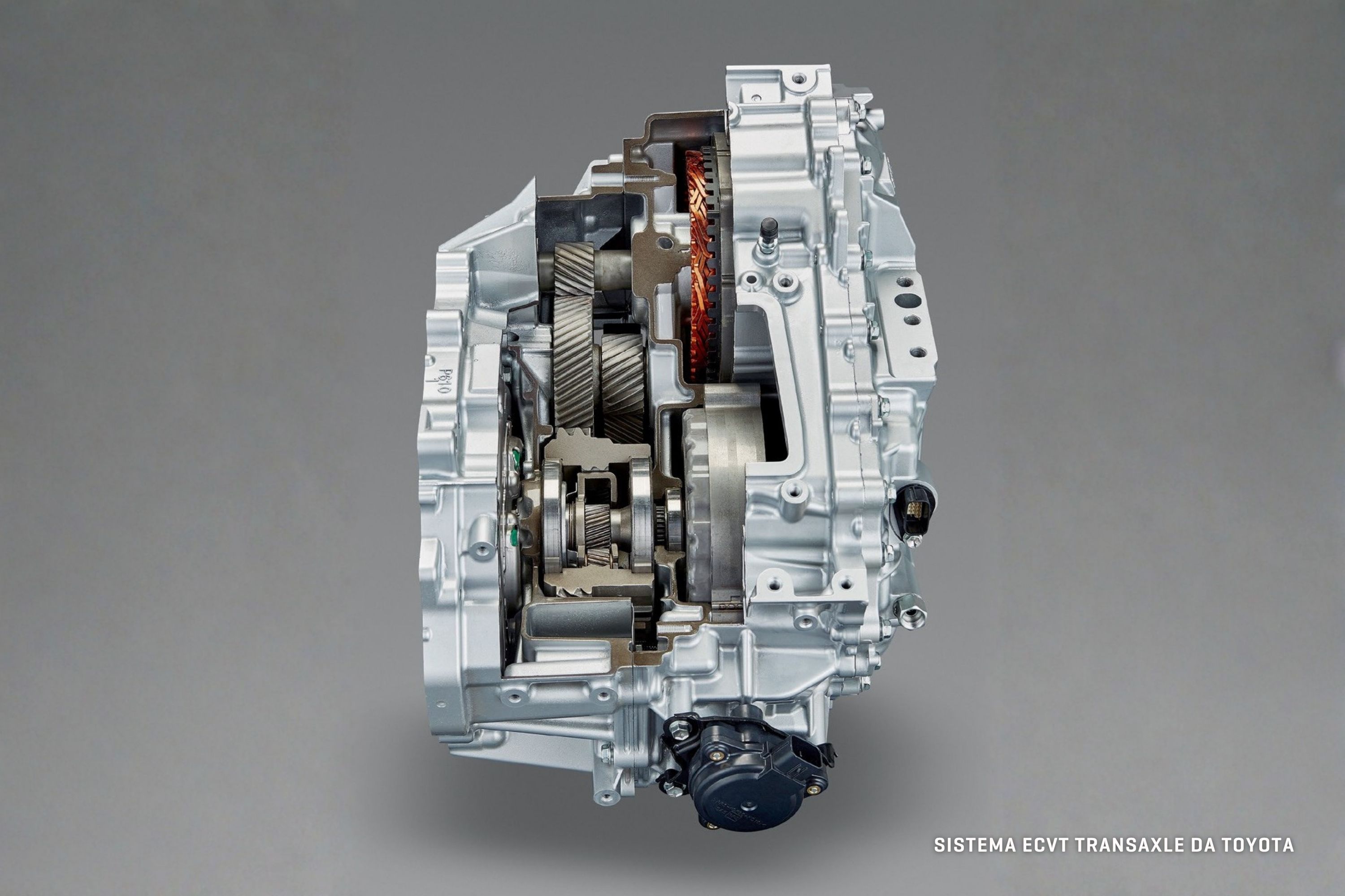 Transmissão eCVT Transaxle da Toyota, com carcaça prateada cortada ao meio, revelando engrenagens, bobinas de cobre e componentes internos em tons de cinza e preto, sobre fundo cinza liso