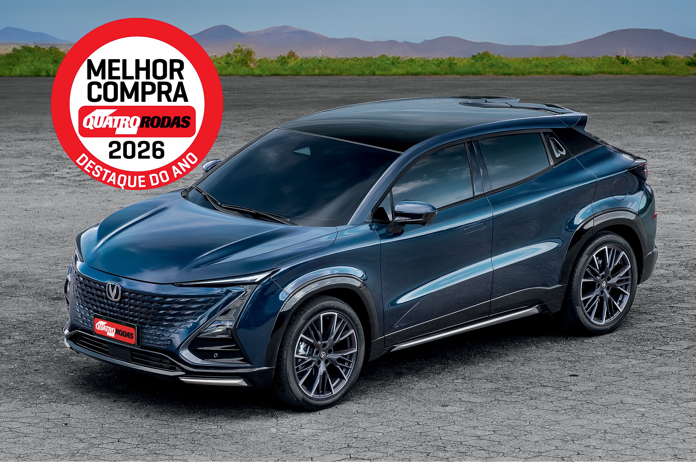 SUV azul escuro, com teto preto e rodas esportivas, estacionado em uma superfície cinza. No canto superior esquerdo, um selo vermelho e branco indica MELHOR COMPRA QUATRO RODAS 2026 DESTAQUE DO ANO. Ao fundo, montanhas e vegetação verde sob um céu azul