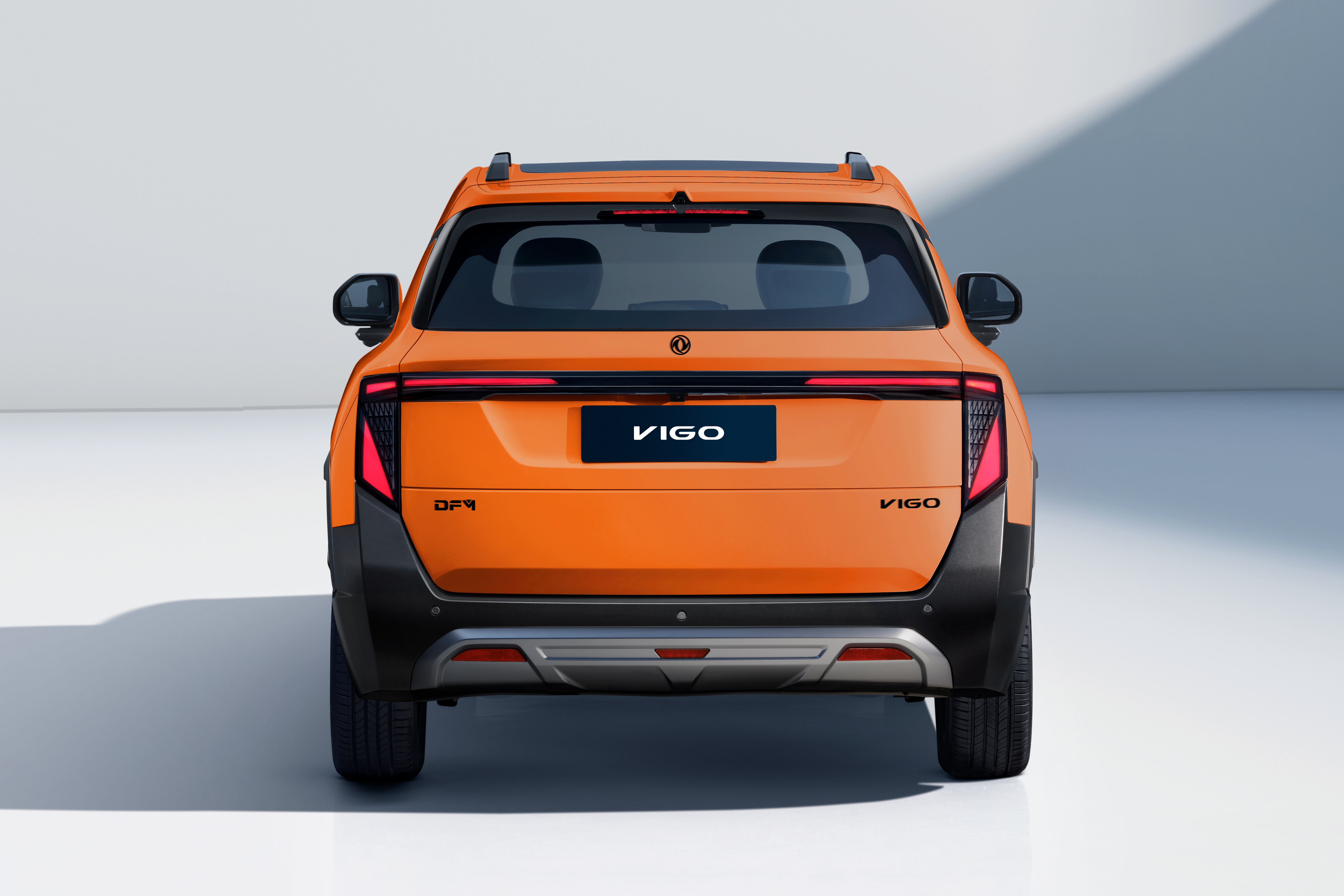 Traseira de um carro laranja VIGO, com detalhes em preto fosco e um para-choque prateado. As lanternas verticais têm luzes vermelhas acesas, e o nome VIGO aparece na placa e no canto inferior direito da tampa do porta-malas. O veículo está em um estúdio branco com sombras suaves