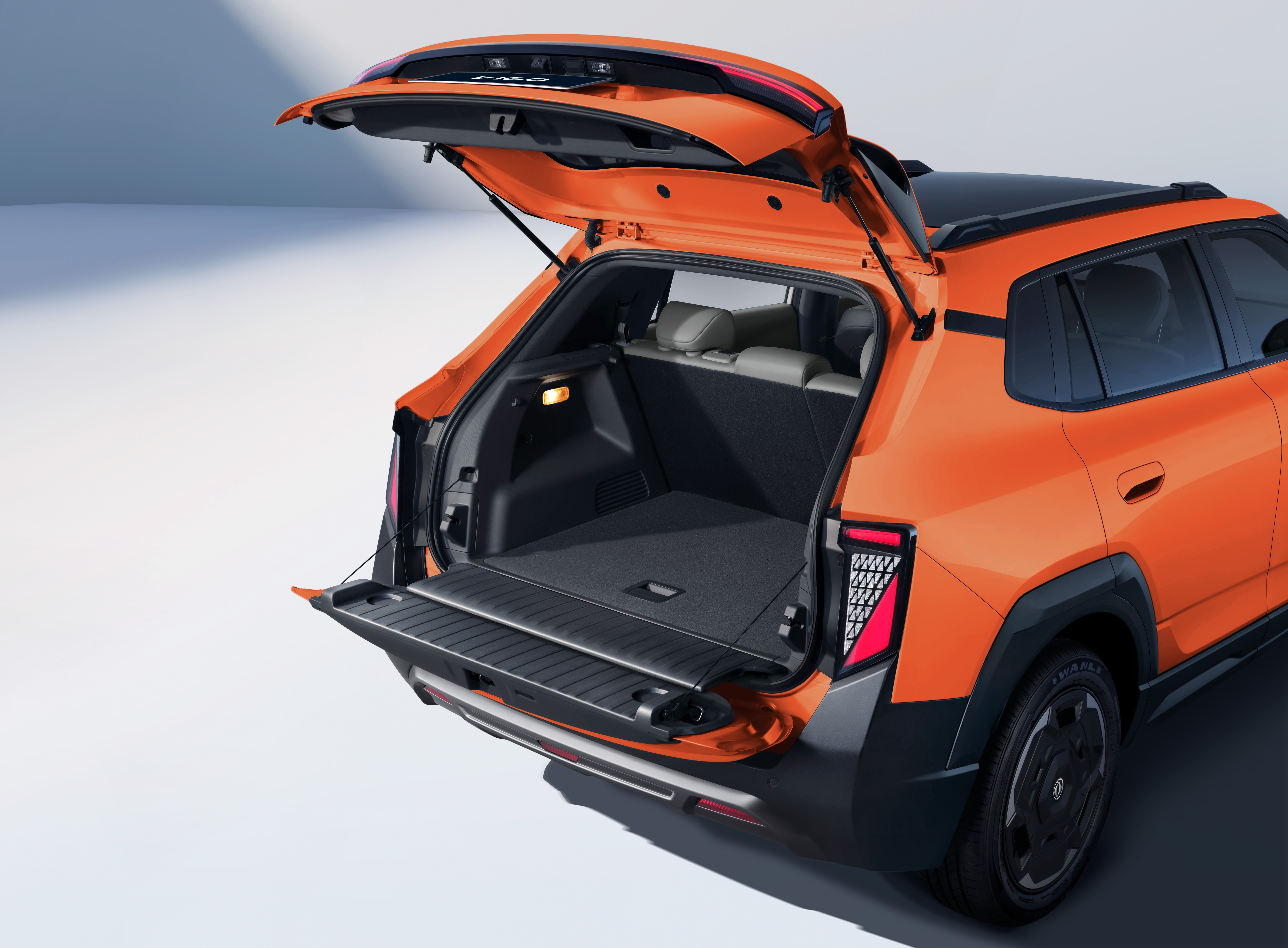 Traseira de um SUV laranja com a tampa do porta-malas aberta, revelando um amplo espaço interno e uma prateleira retrátil. As lanternas traseiras têm design moderno e o para-choque é preto com detalhes prateados. O veículo está em um estúdio com fundo claro