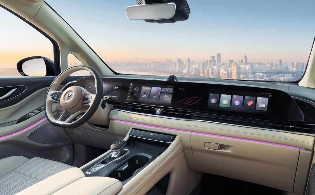 Interior de um carro moderno com painel digital e volante bege, detalhes em rosa neon e bancos claros. Ao fundo, uma cidade com arranha-céus sob céu azul
